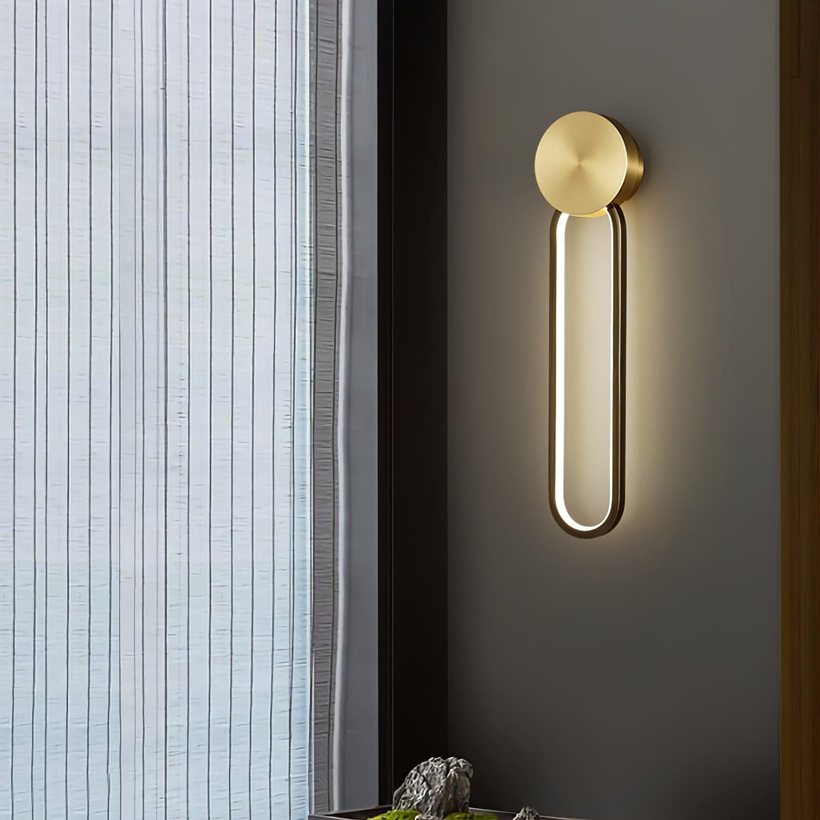Angled view of the lit black oval loop and brass-tone disc beside a sheer window covering