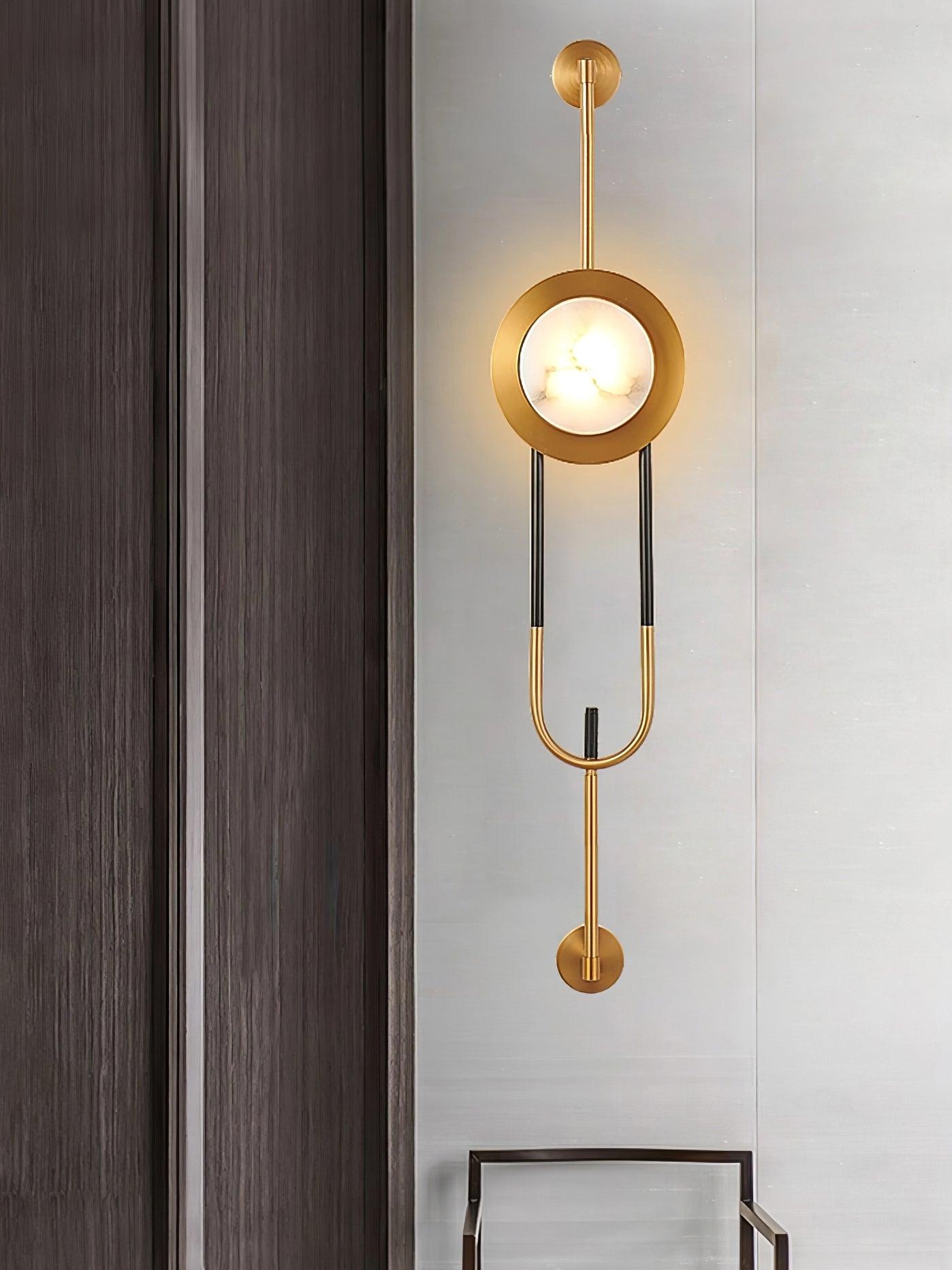 Illuminated marble disc and gold loop-frame wall light on dark wood paneling above a chair