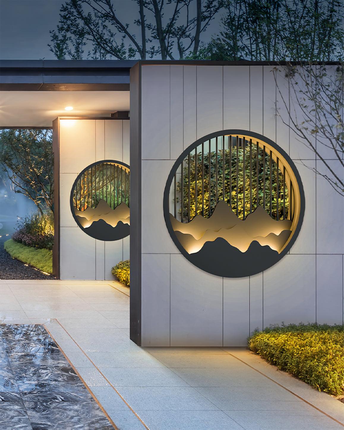 Two circular mountain lights on pale panelled garden-entrance walls, with water surface and planting beside the path