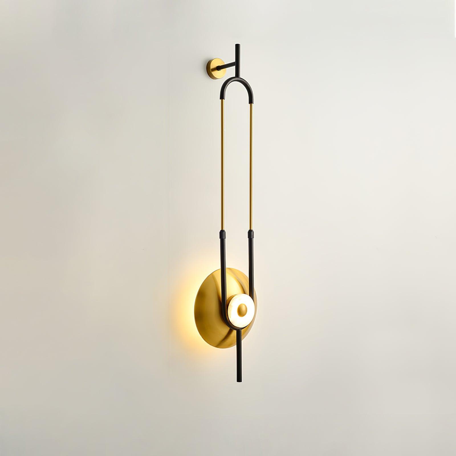 Close oblique wall light with round upper gold mount, black support and warm wall halo behind gold disc