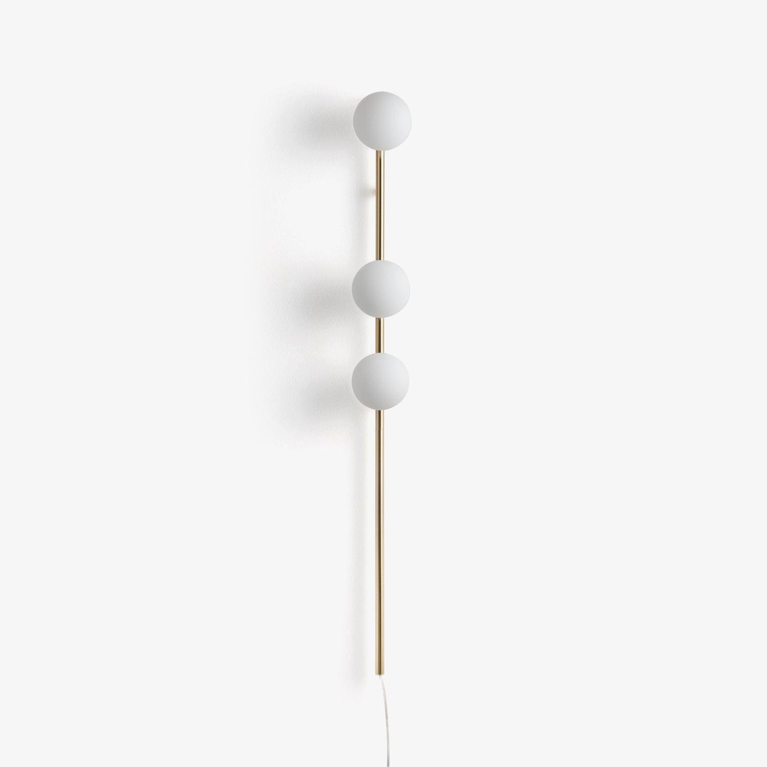 Front view of unlit Gold three-globe wall light on pale wall, slim metal stem and pale trailing cord