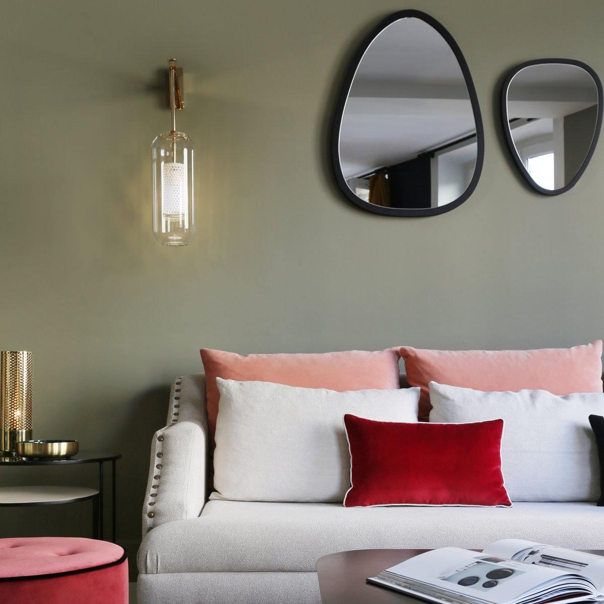 Clear glass wall light beside two irregular rounded mirrors above a sofa