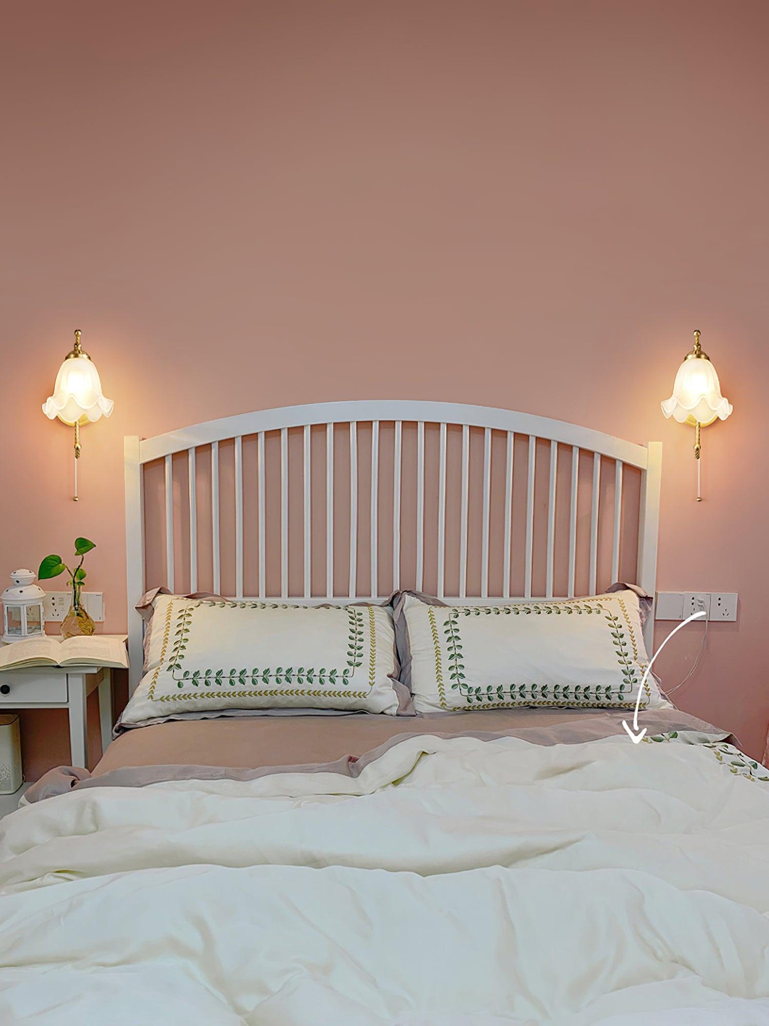 Two matching floral glass wall lamps flanking white slatted headboard on pink wall, with a white arrow annotation over the bedding