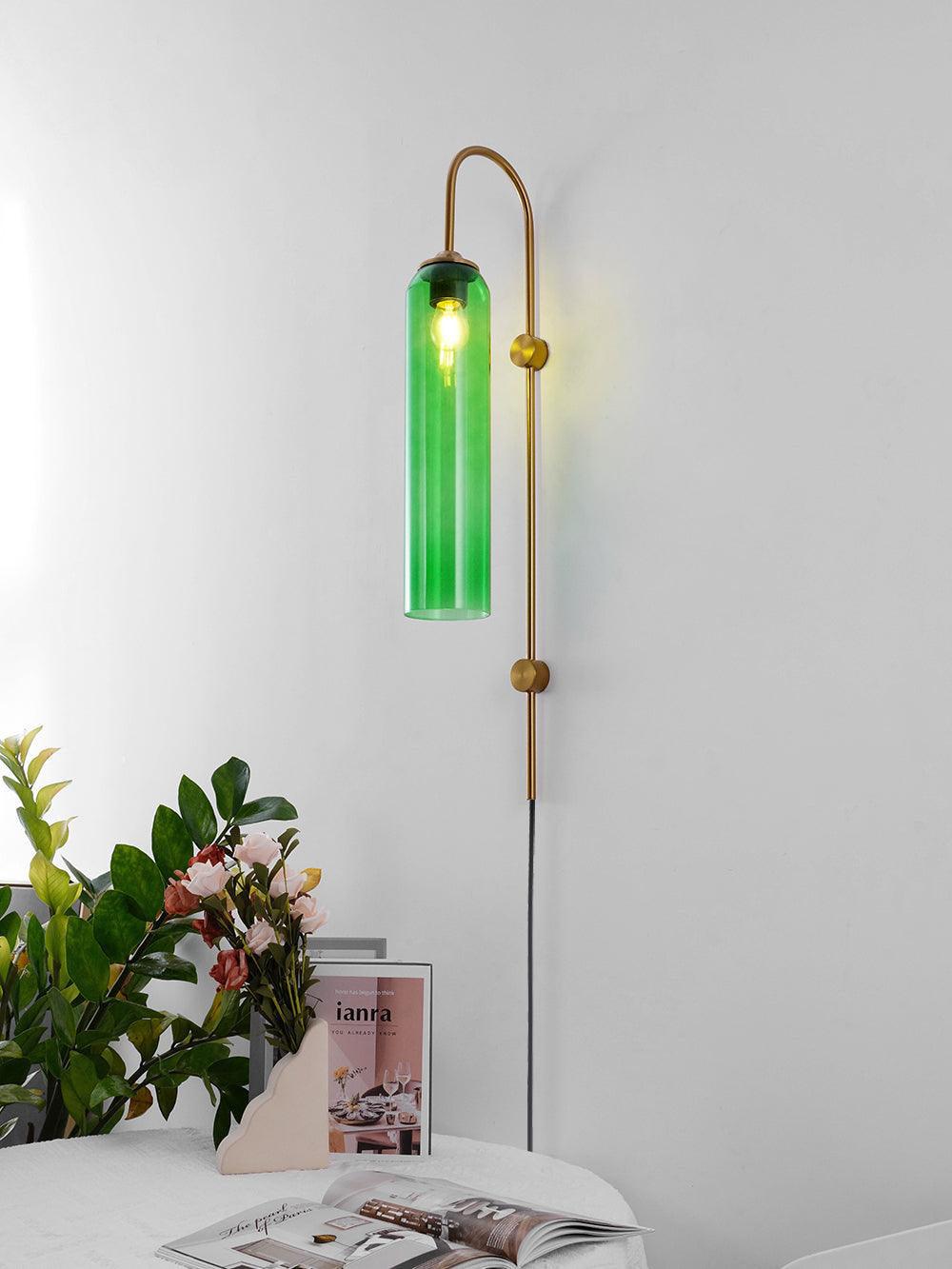 Green cylindrical glass wall lamp above flowers and a cloth-covered table