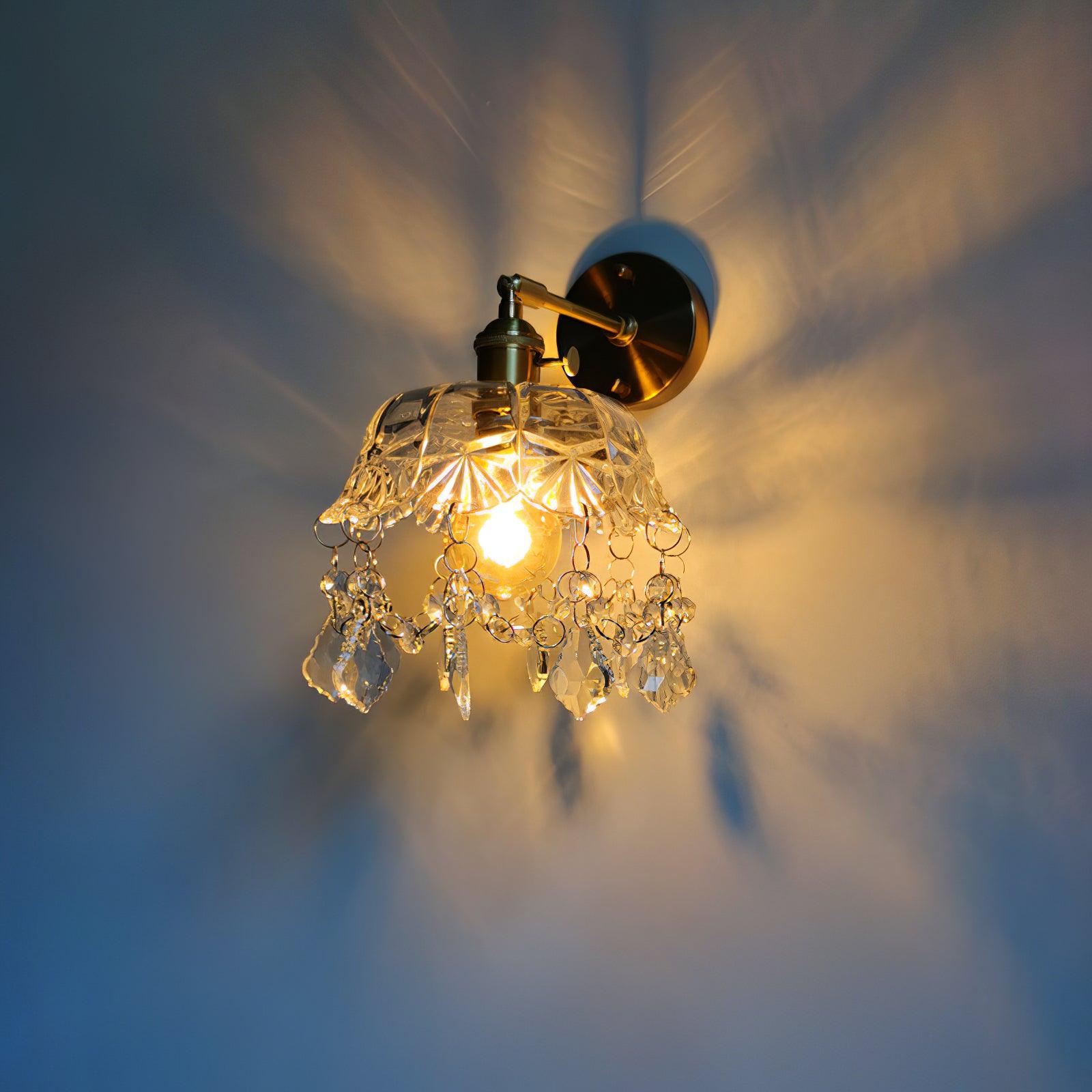 Angled lit crystal-fringed wall light with a gold-tone wall plate and patterned illumination on a dark wall