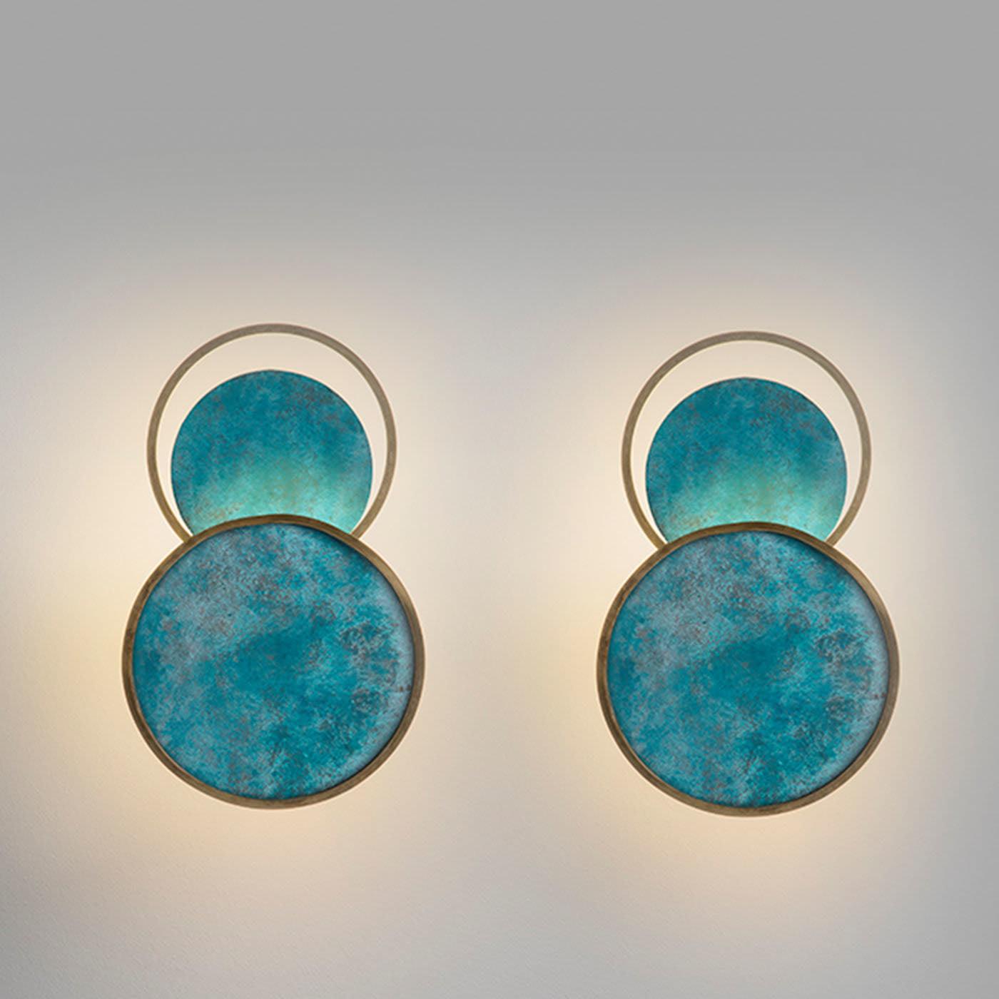 Two turquoise circular wall lights on a pale wall, showing open upper rings and side-lit halos around the blue faces.