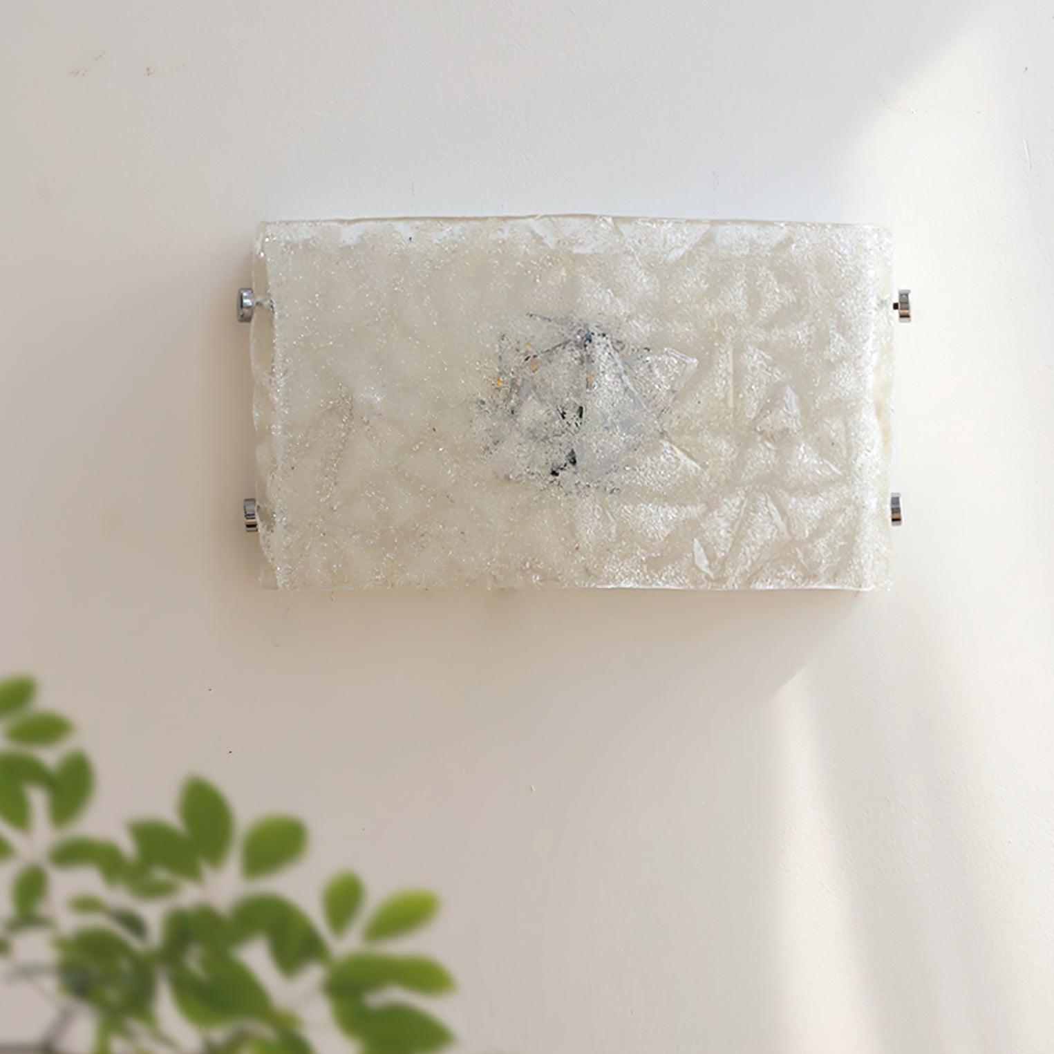Front close-up of unlit textured glass wall light with irregular darker bands and four chrome edge fasteners