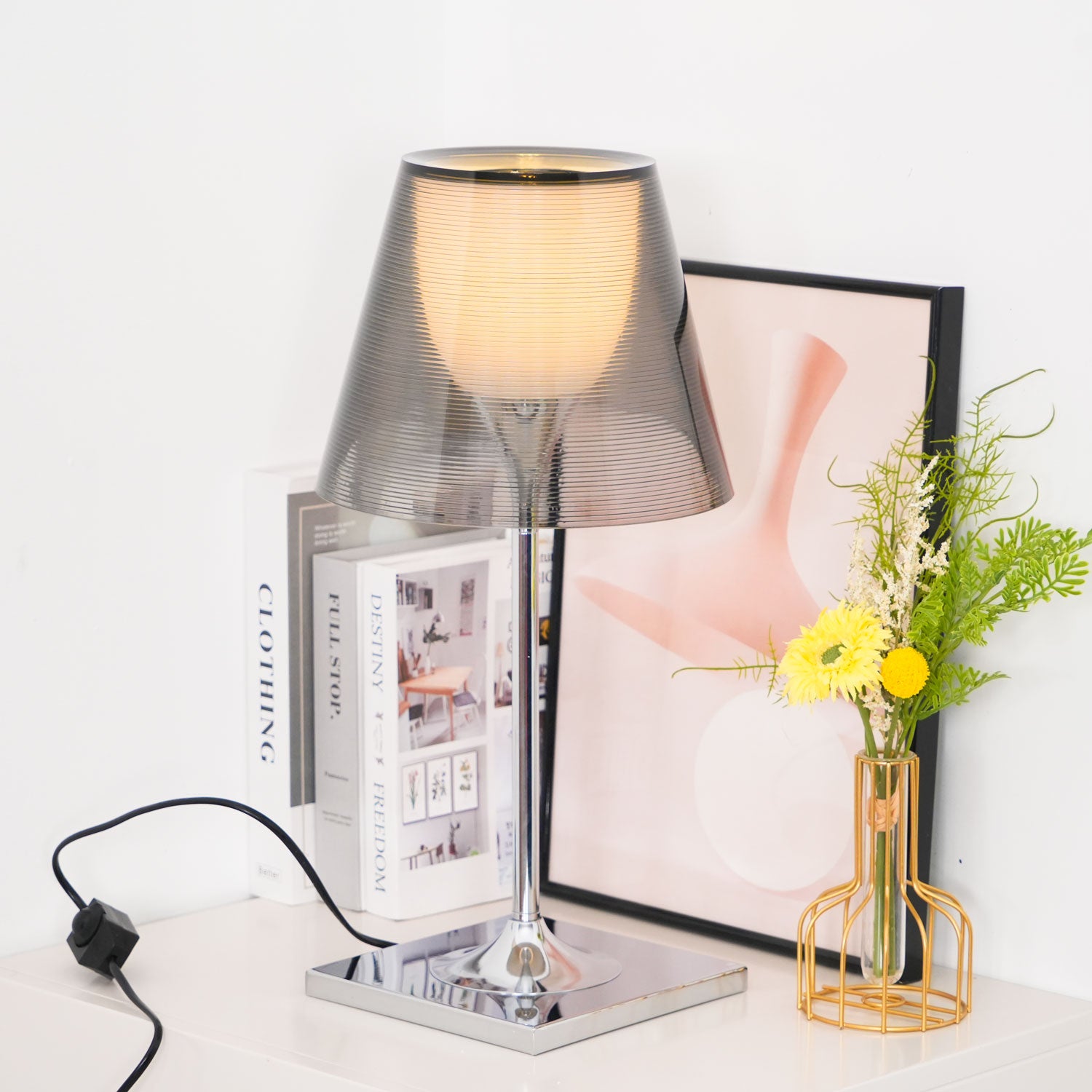 Chrome Prism lamp glowing beside books and yellow flowers