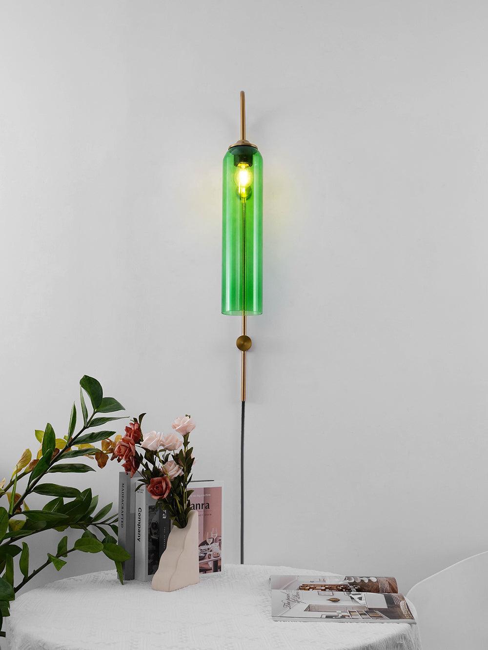 Green glass tube on a slim metal wall stem above a floral arrangement