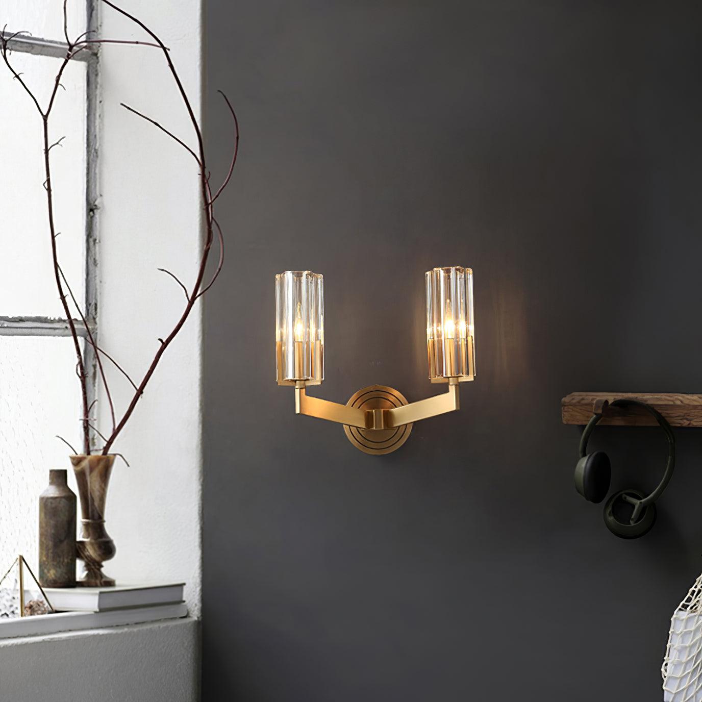 Twin-shade Kayla light on grey wall beside window, branch vases, books and hanging headphones, with brass arms and clear glass