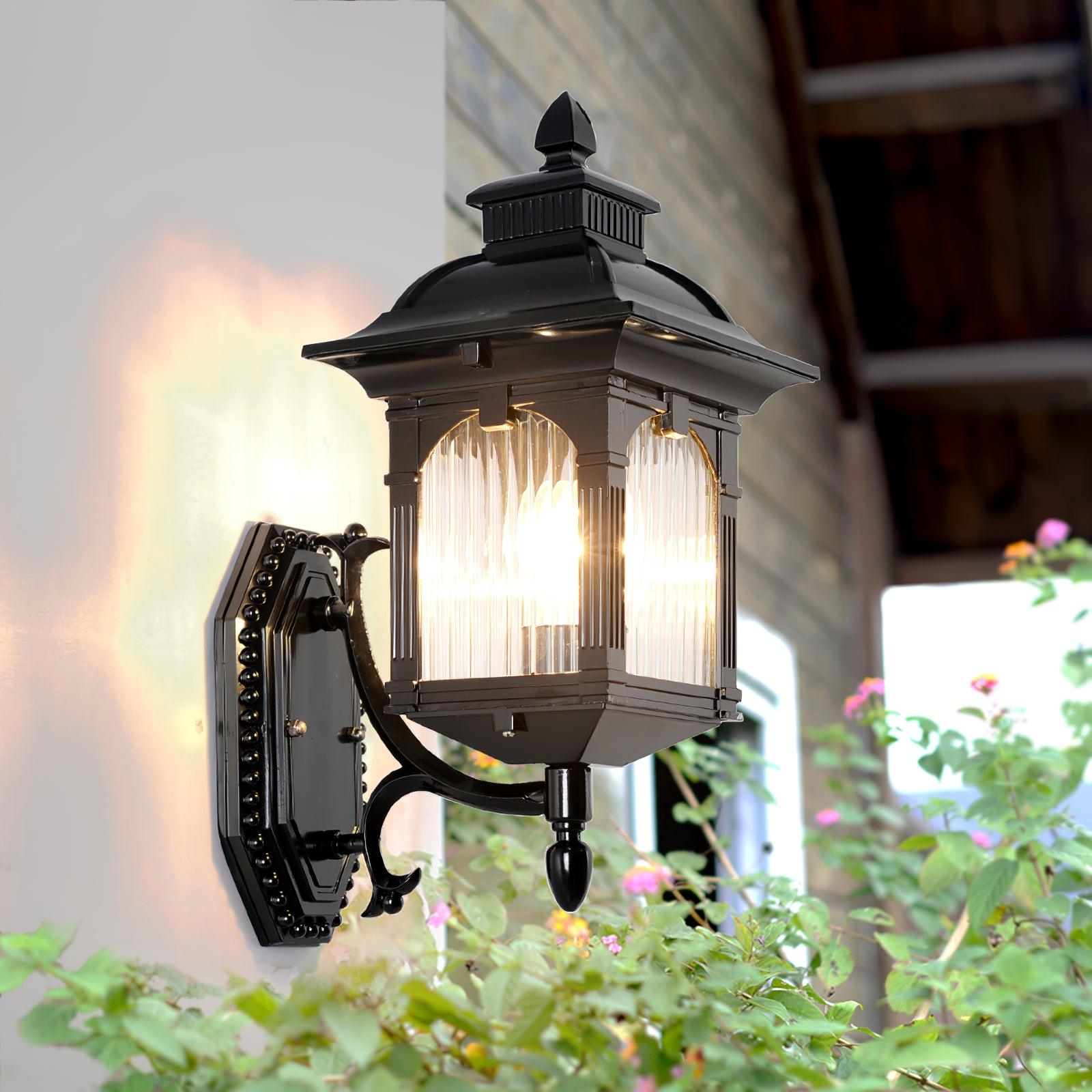 Black Miller lantern lit beside greenery on an outdoor wall