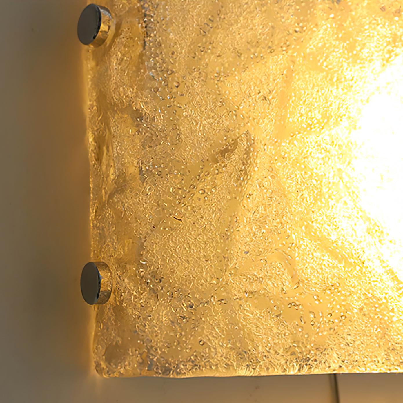 Close-up of the lit left glass edge with fine texture, two chrome fasteners and a warm-looking glow to the right