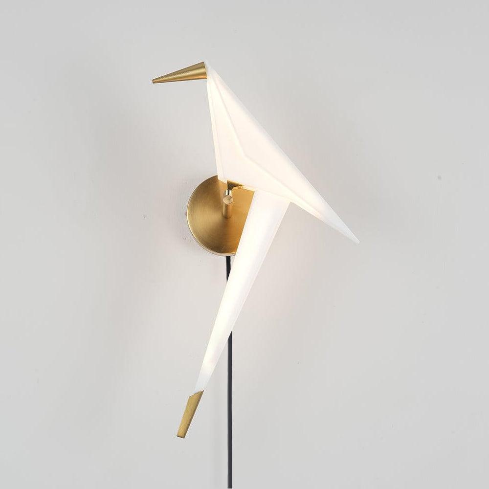 White origami-shaped bird wall light with Gold beak, tail tip and round backplate, with a Black cable against a pale wall