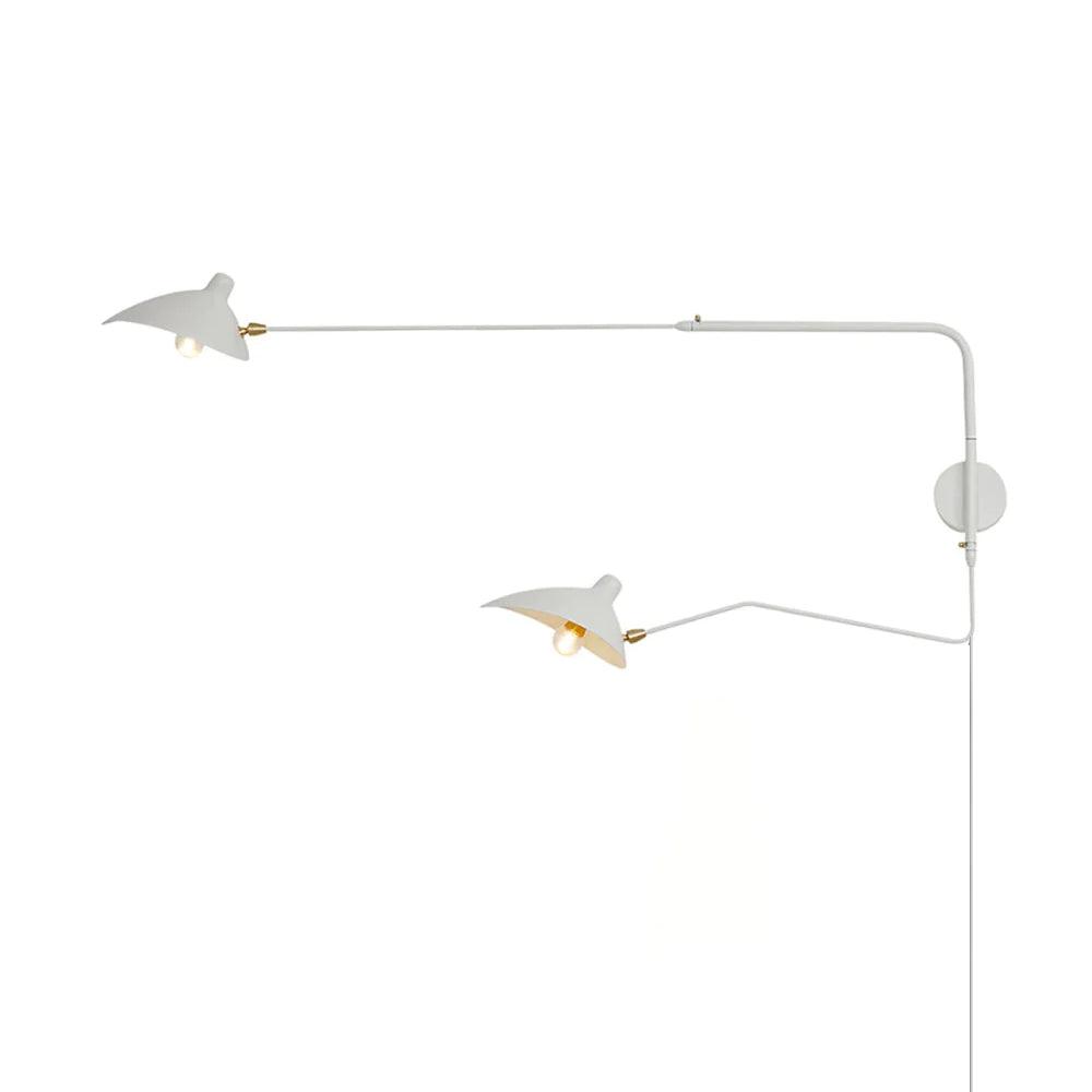 White two-head wall lamp with long upper and shorter lower arms, two lit shades, gold-tone joints and one round wallplate