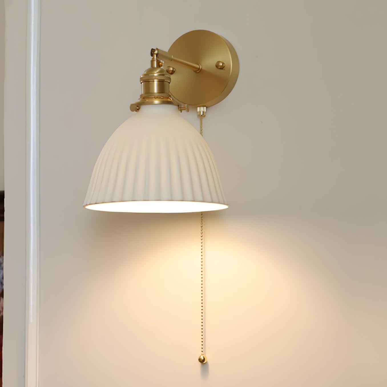 Close angled view of lit ceramic pleats, brass holder and wall plate, with a long round-ended chain