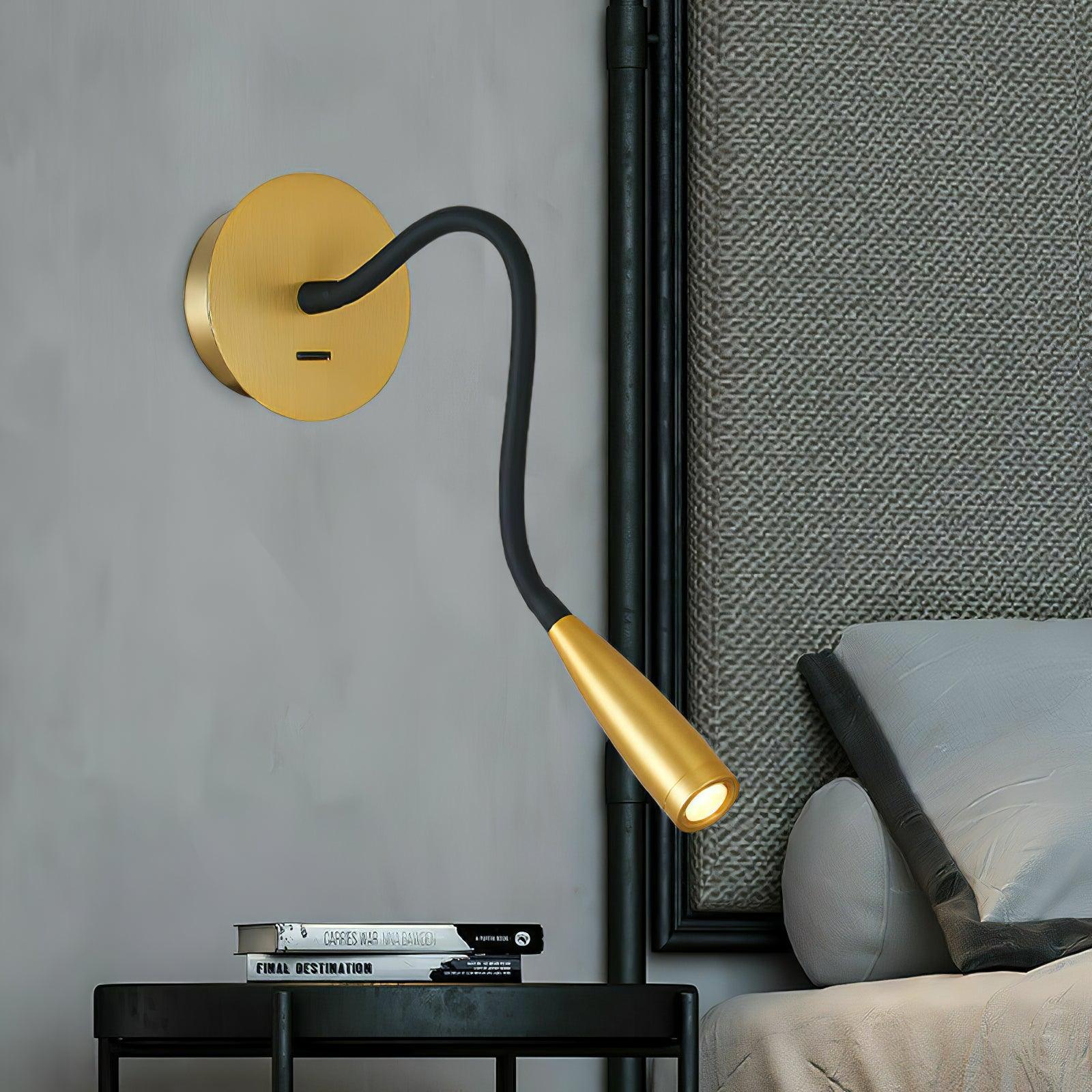 Close gold wall light with glowing tapered head beside grey headboard and books on black bedside table
