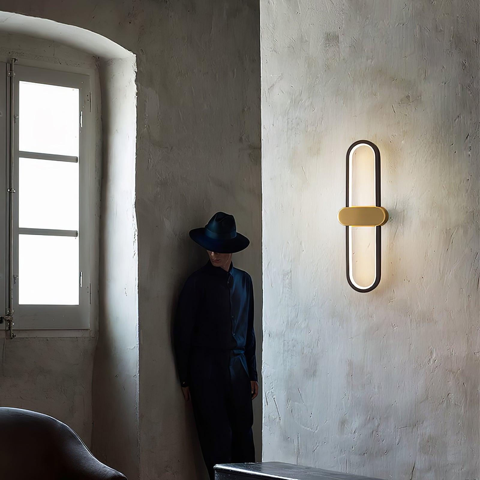 Black oval wall light with gold-coloured centre on a textured white wall beside a person in a dark hat