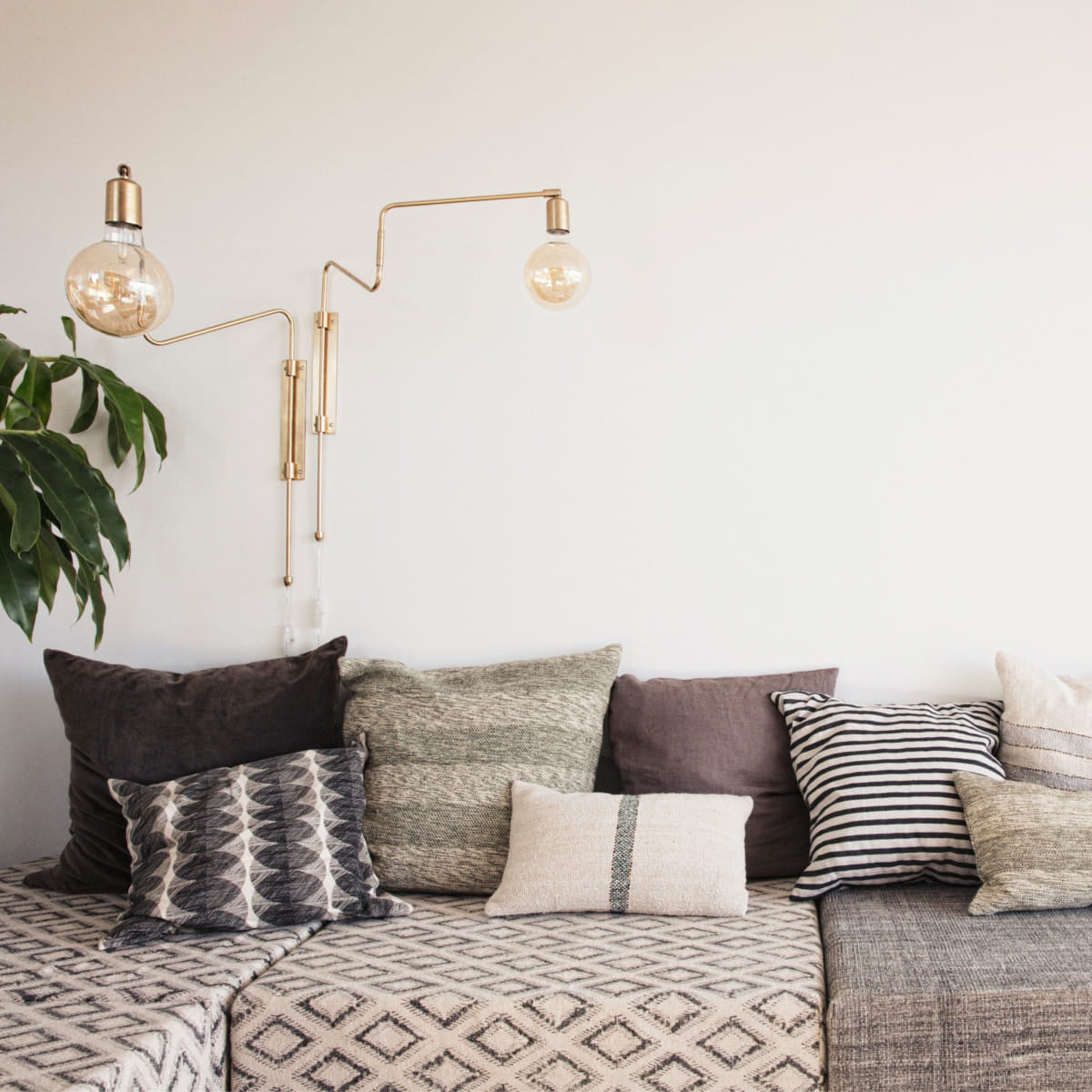 Brass swing-arm fixture above sofa cushions