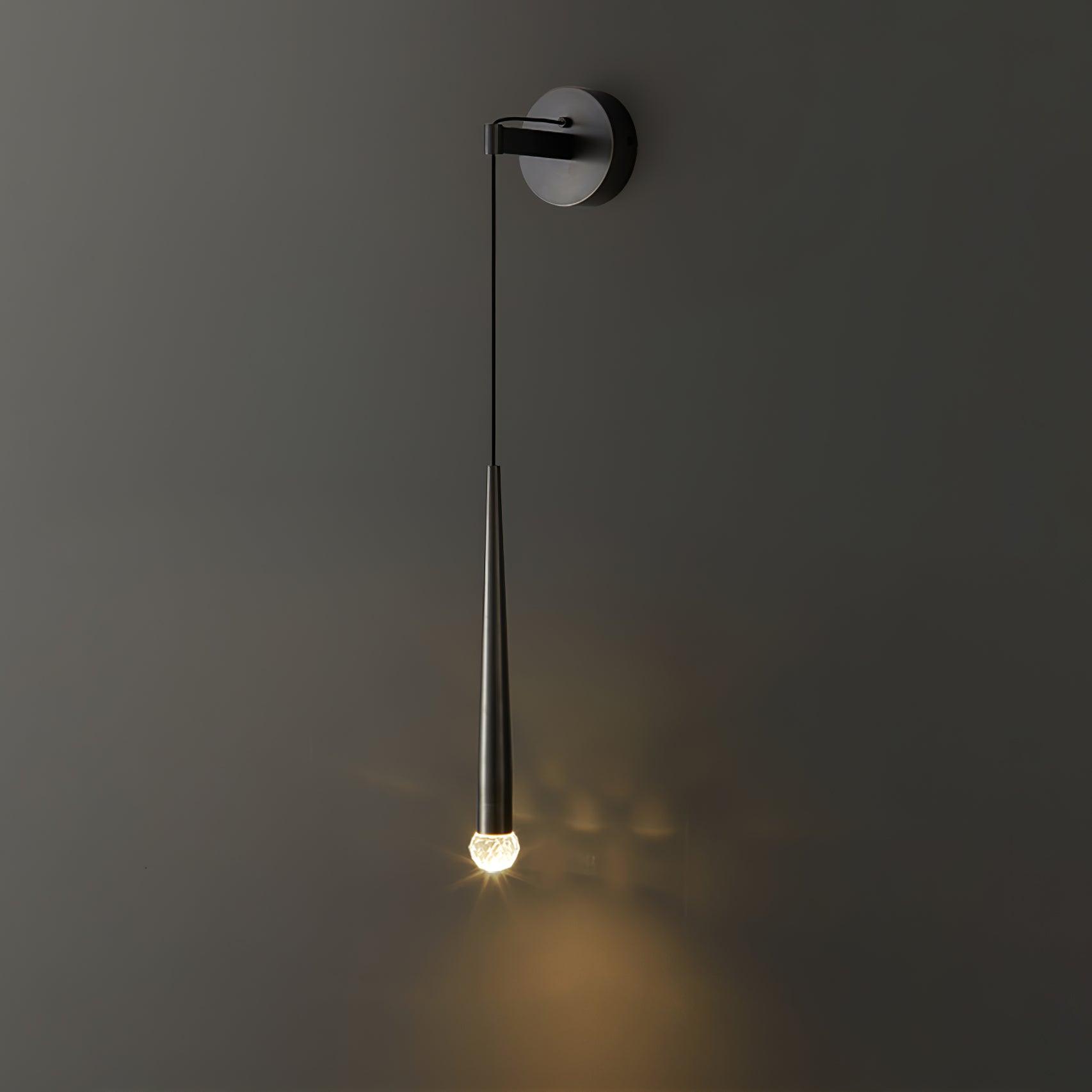 Lit black conical wall light with a faceted crystal tip casting a pattern on a dark-grey wall
