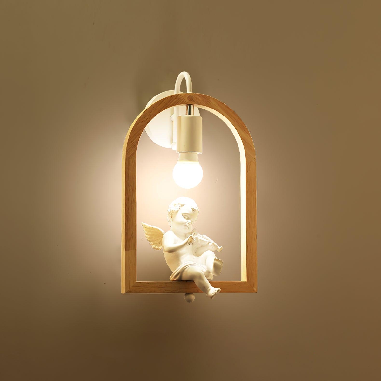 Close front view of the lit cherub wall light, showing violin, wings and one foot extending below the wooden frame