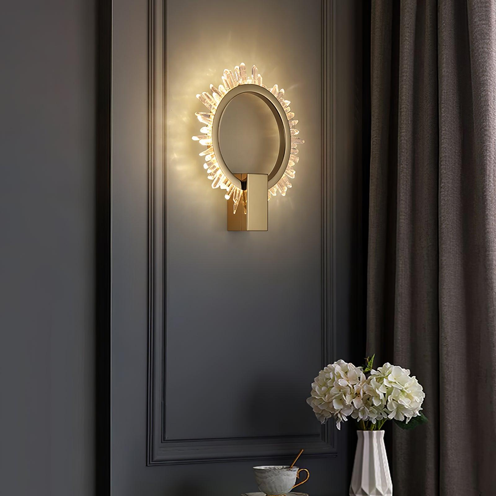 Lit gold crystal ring wall lamp on dark panelling above a vase of white flowers and a cup