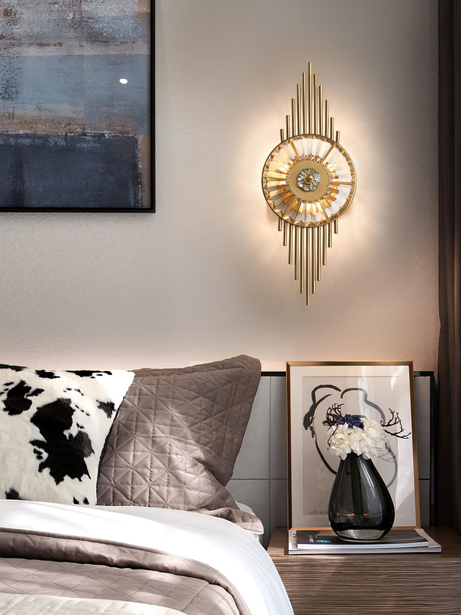 Gold and clear glass wall lamp beside a bed, flowers in a dark vase and framed artwork