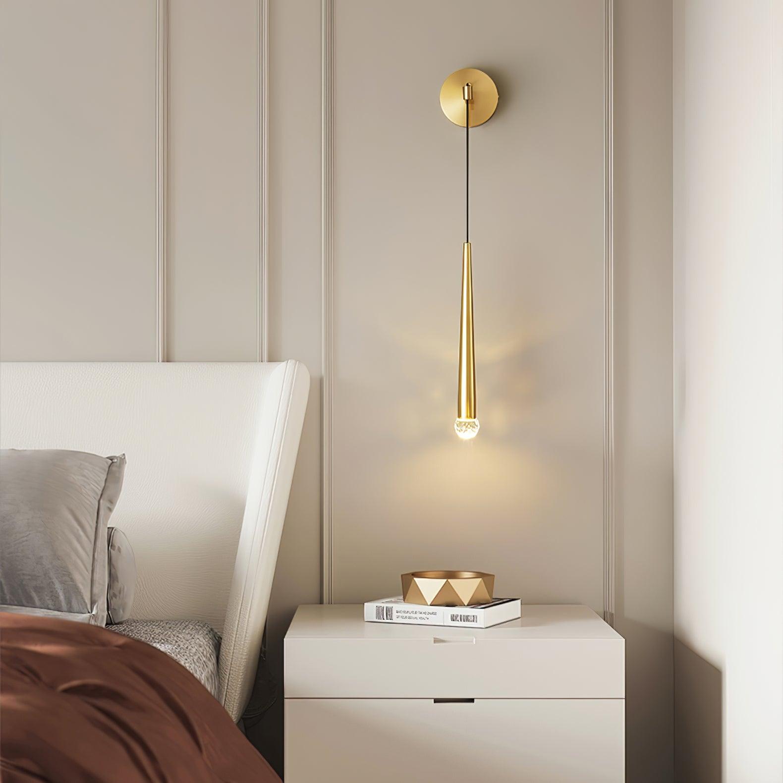 Brass-tone crystal-tipped hanging wall light above white bedside drawers beside a white headboard