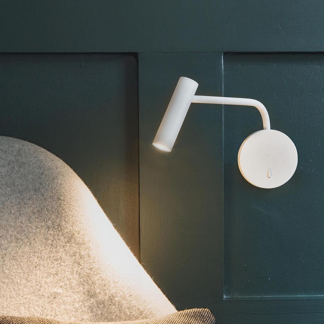 White reading light beside a chair and dark panelling