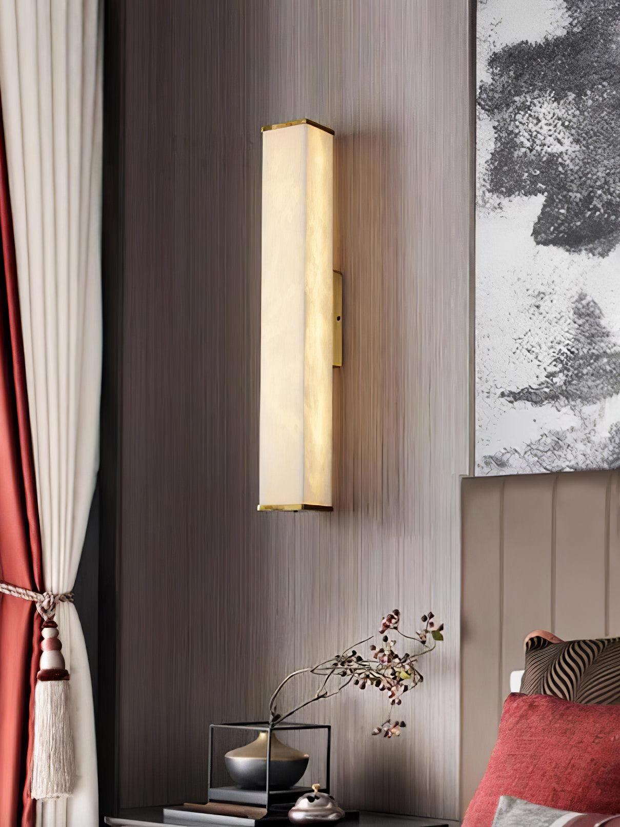 Closer bedroom view of the lit alabaster wall light beside tied curtains, monochrome artwork and a flower branch vase