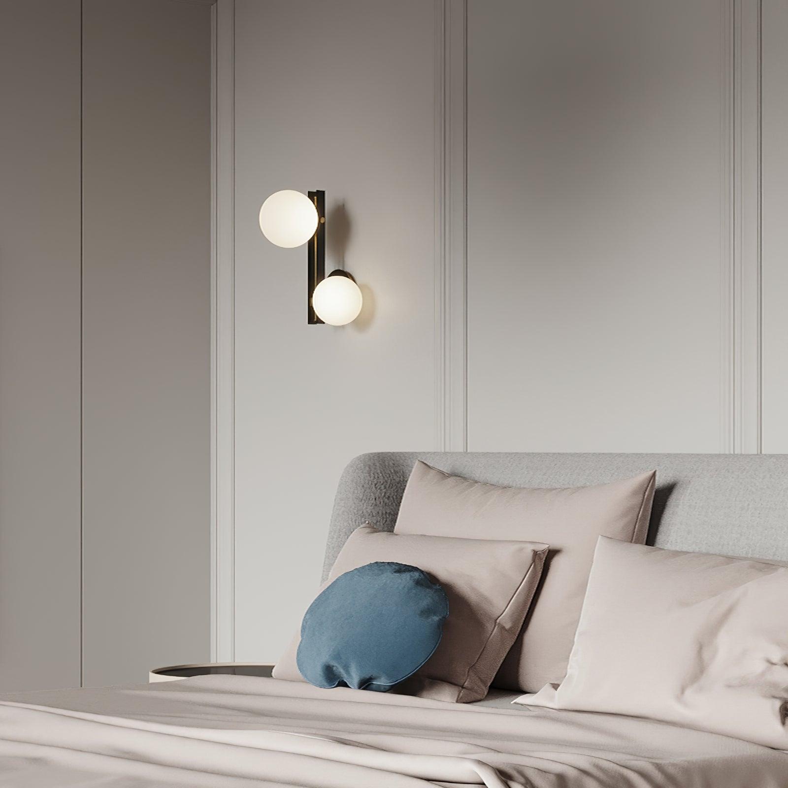 Single two-globe wall light above an upholstered headboard and cushions on a pale panelled wall