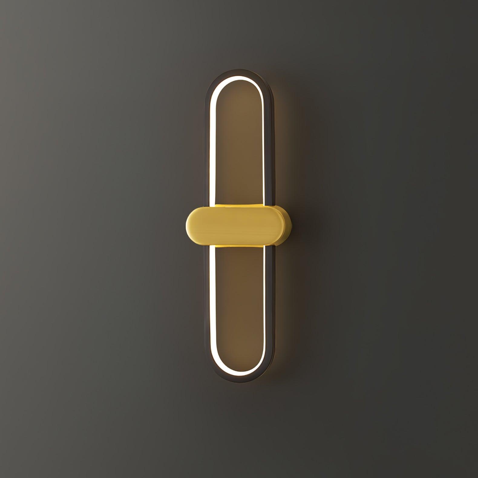 Angled lit view of the black oval wall light with gold-coloured central capsule cover