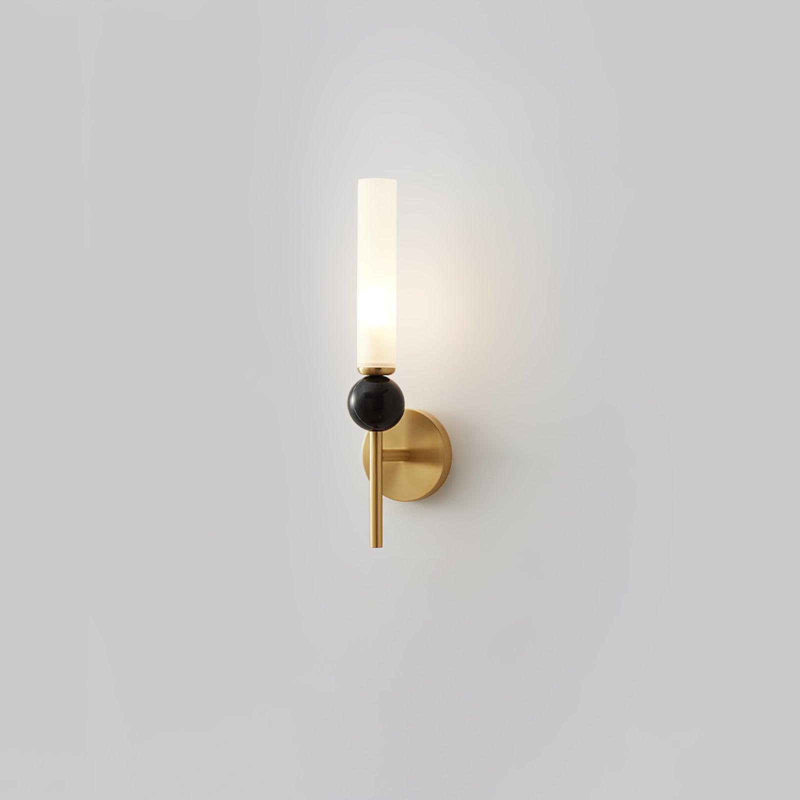 Straight-stem brass wall lamp isolated on pale background, with dark marble sphere and lit upright white acrylic cylinder