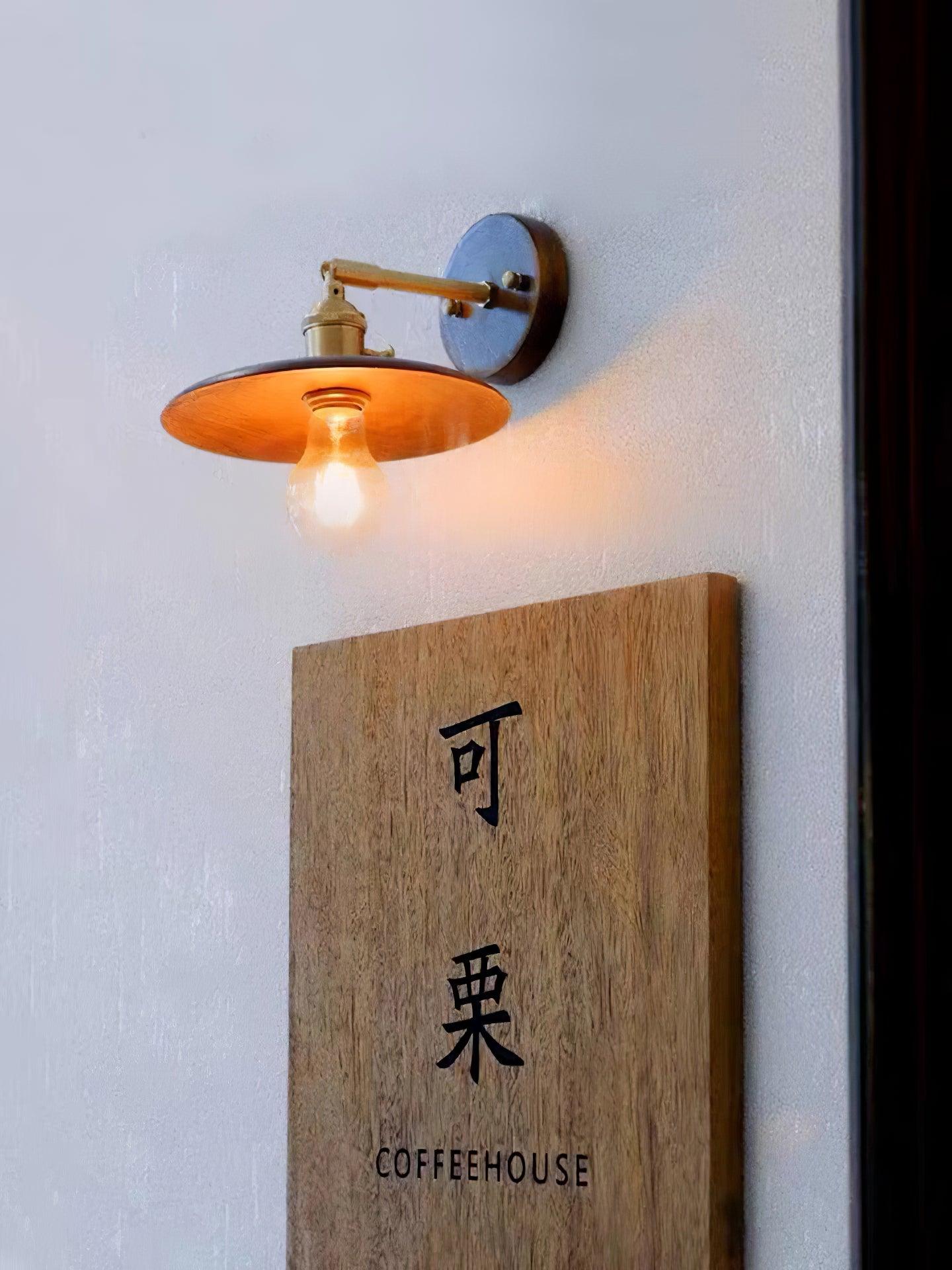 Low view of wooden flared shade and warm bulb above COFFEE HOUSE sign on textured pale wall
