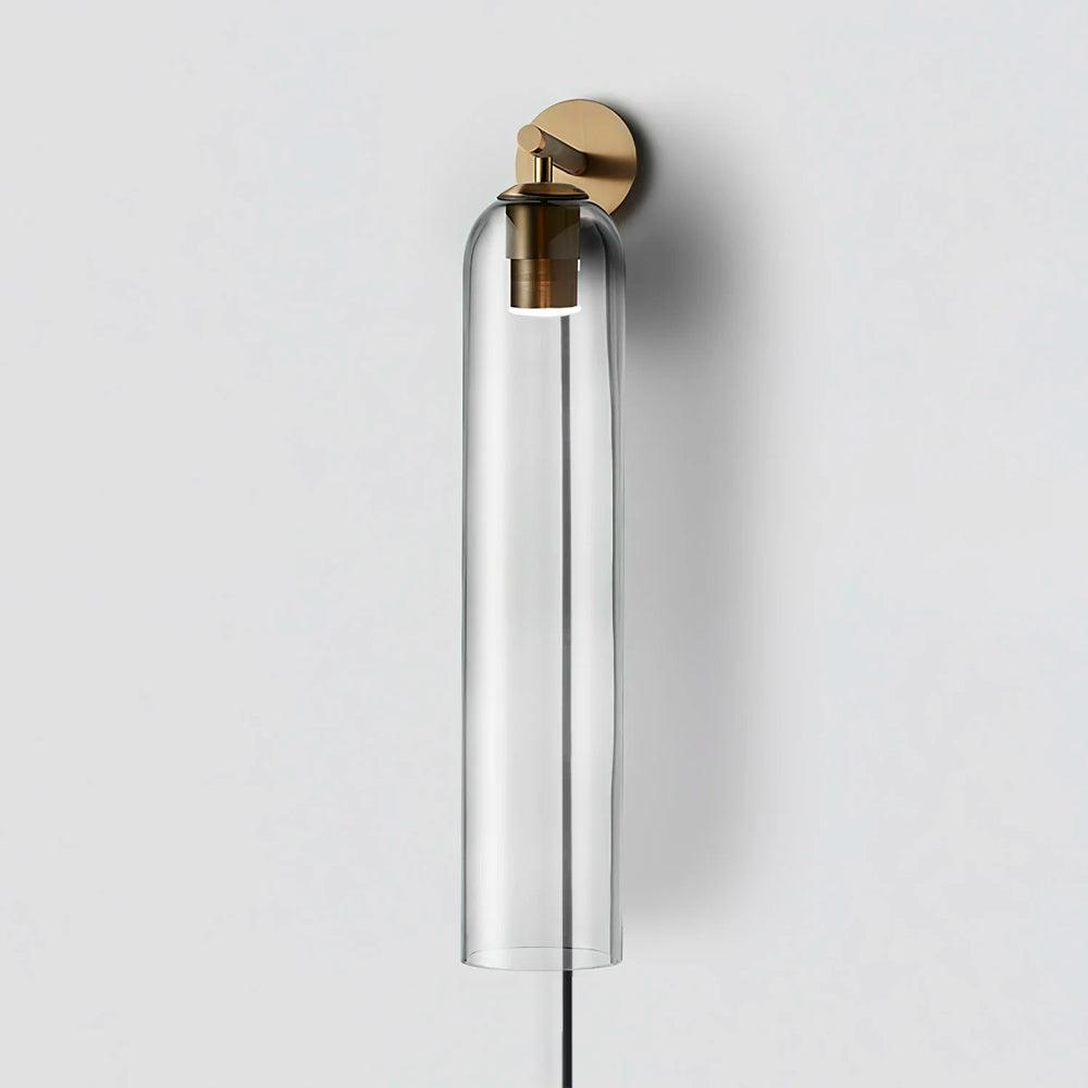 Clear glass cylinder suspended from a short gold arm and round wall plate