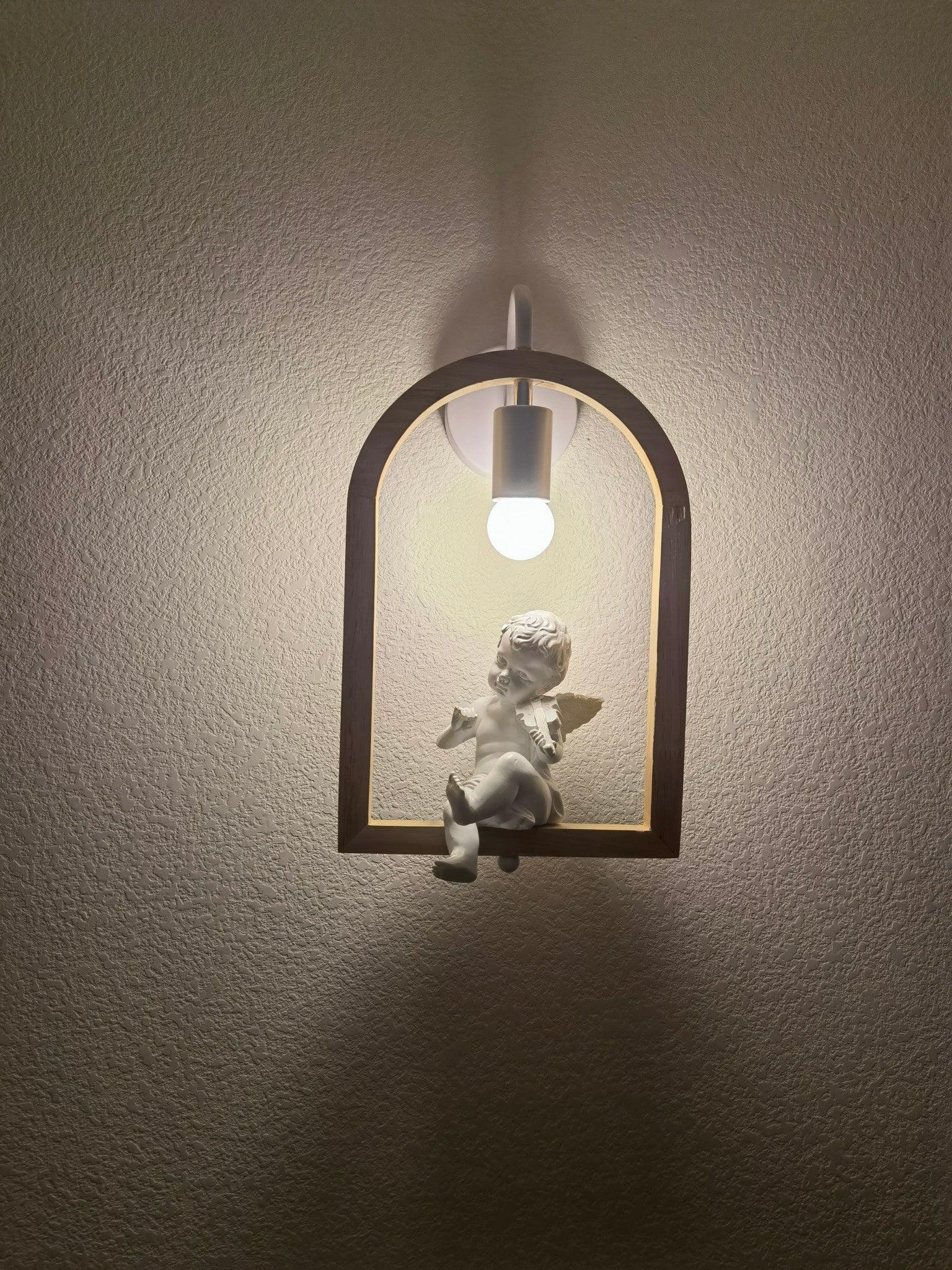 Cherub wall lamp glowing against a textured wall in a dark room, with its arched frame casting a shadow