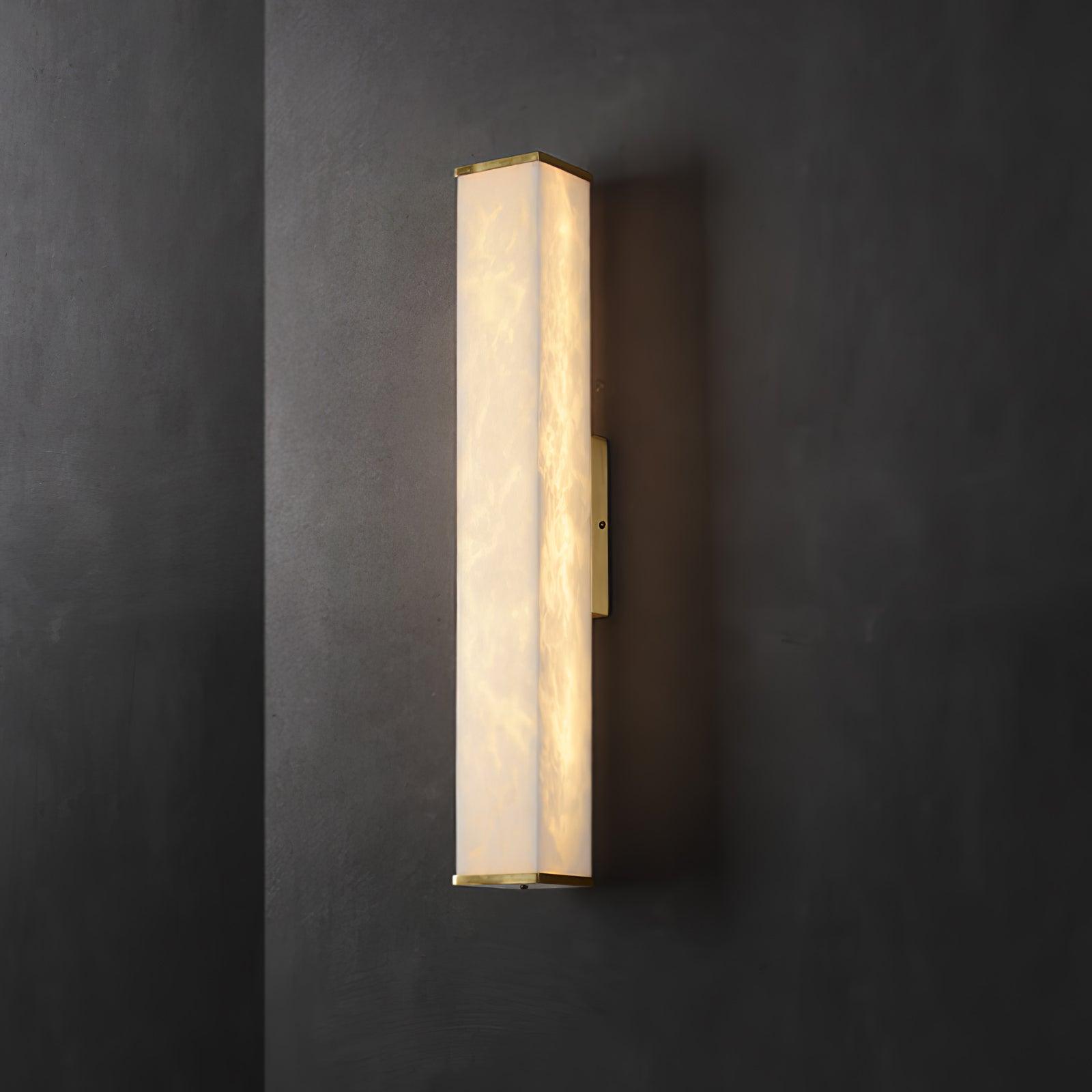 Lit alabaster wall light with brass end caps and a narrow side mounting plate against a dark gray corner wall