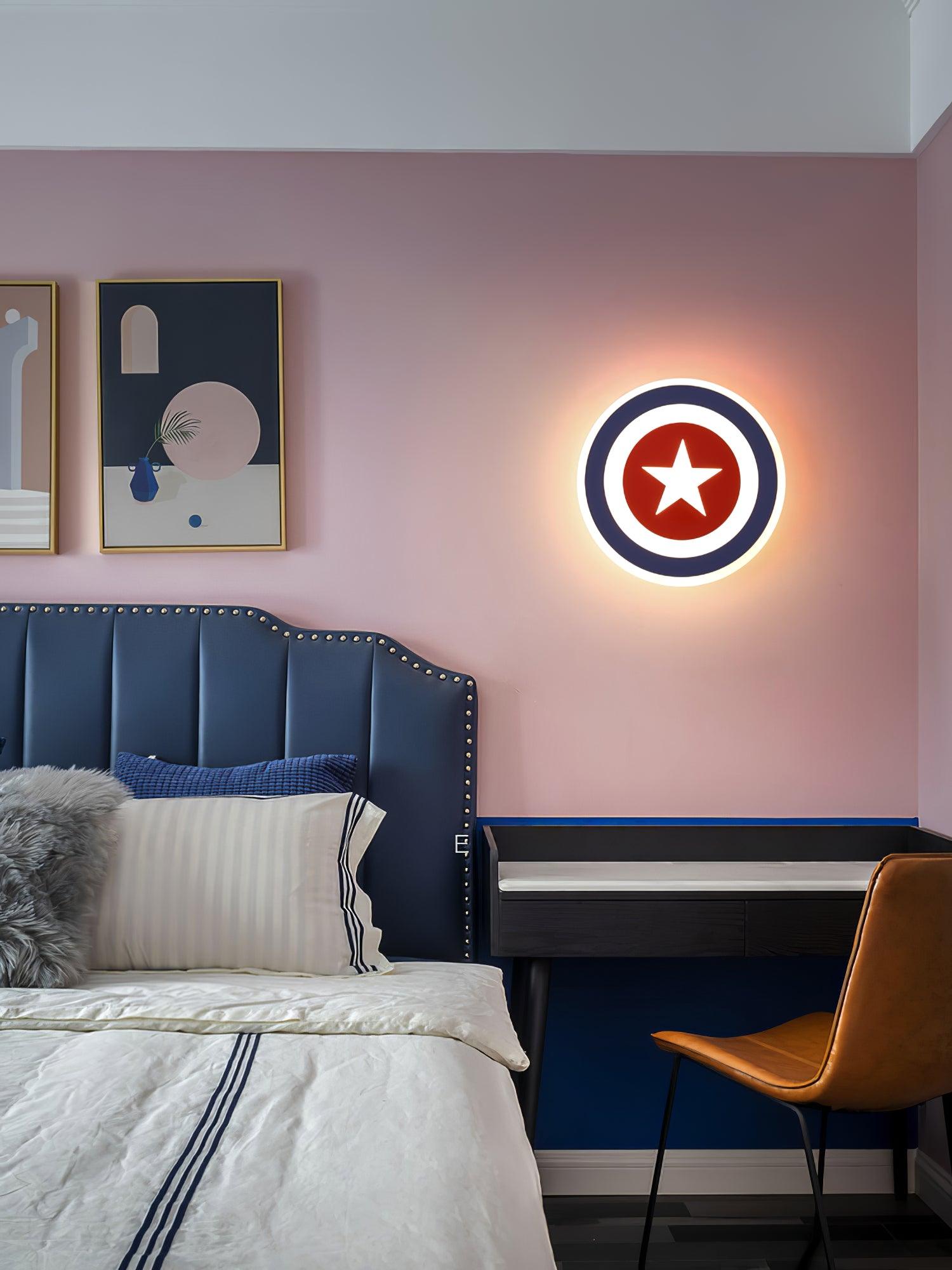 Wide view of blue-ring star lamp on pink wall beside blue upholstered bedhead, framed art and desk