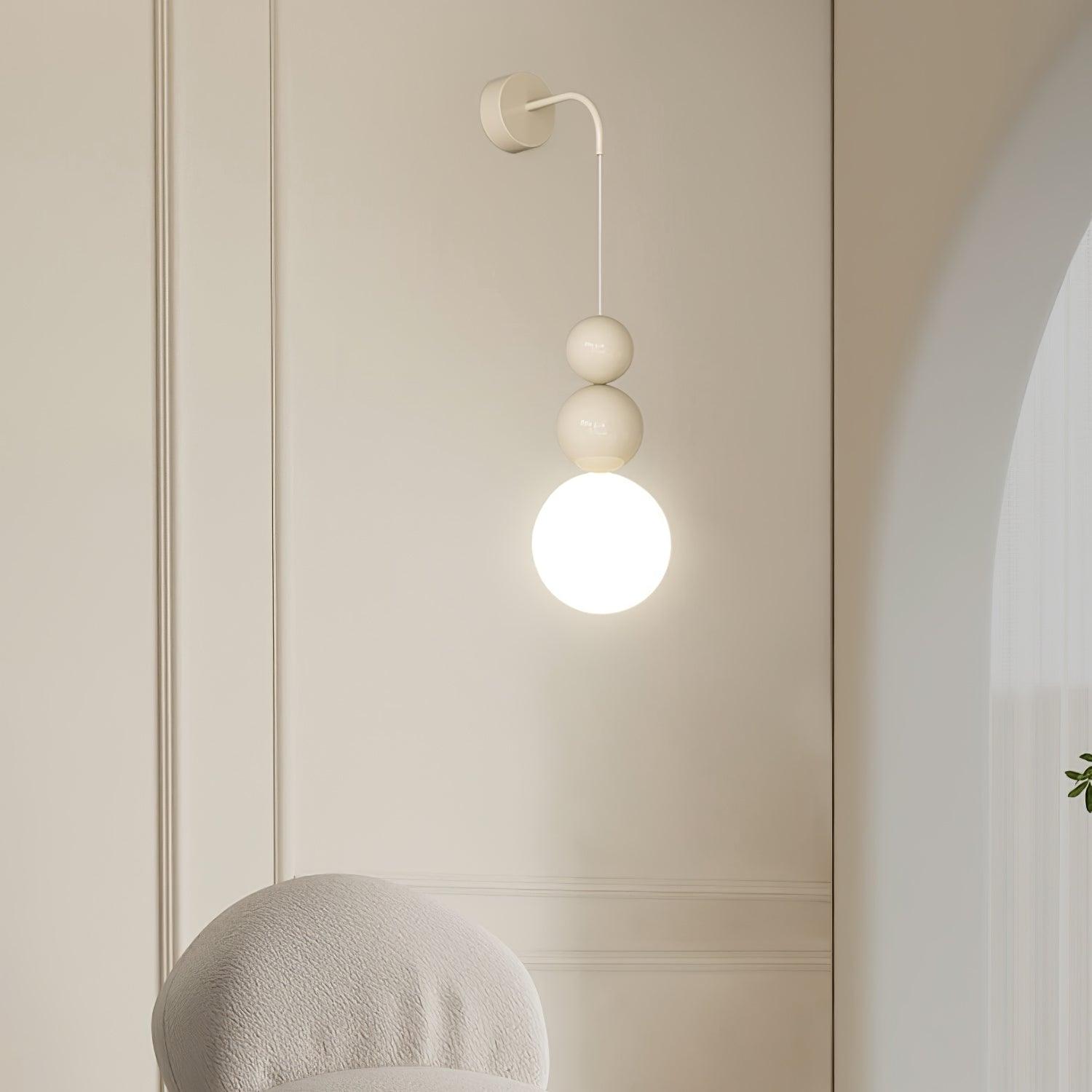 Lit beige Three Ball wall light beside a pale upholstered chair and panelled wall