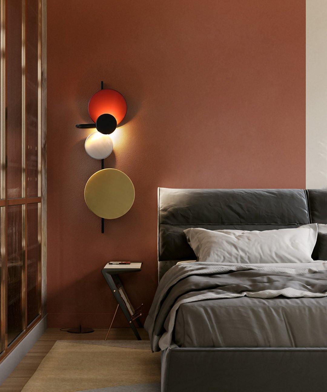 Red disc wall light beside a bed