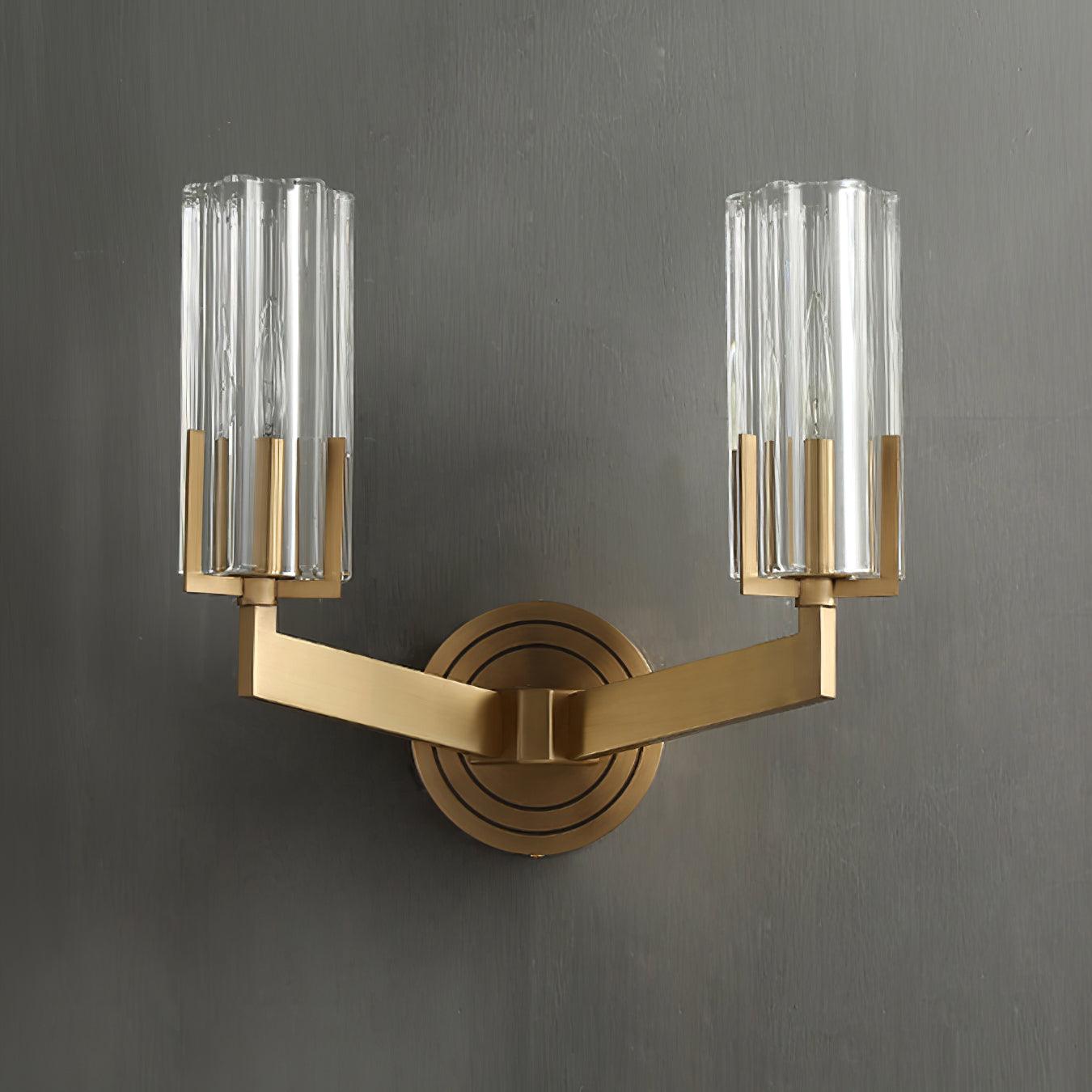 Unlit twin-shade Kayla on grey wall with clear fluted cylinders, visible candle bulbs, brass arms and ringed circular plate