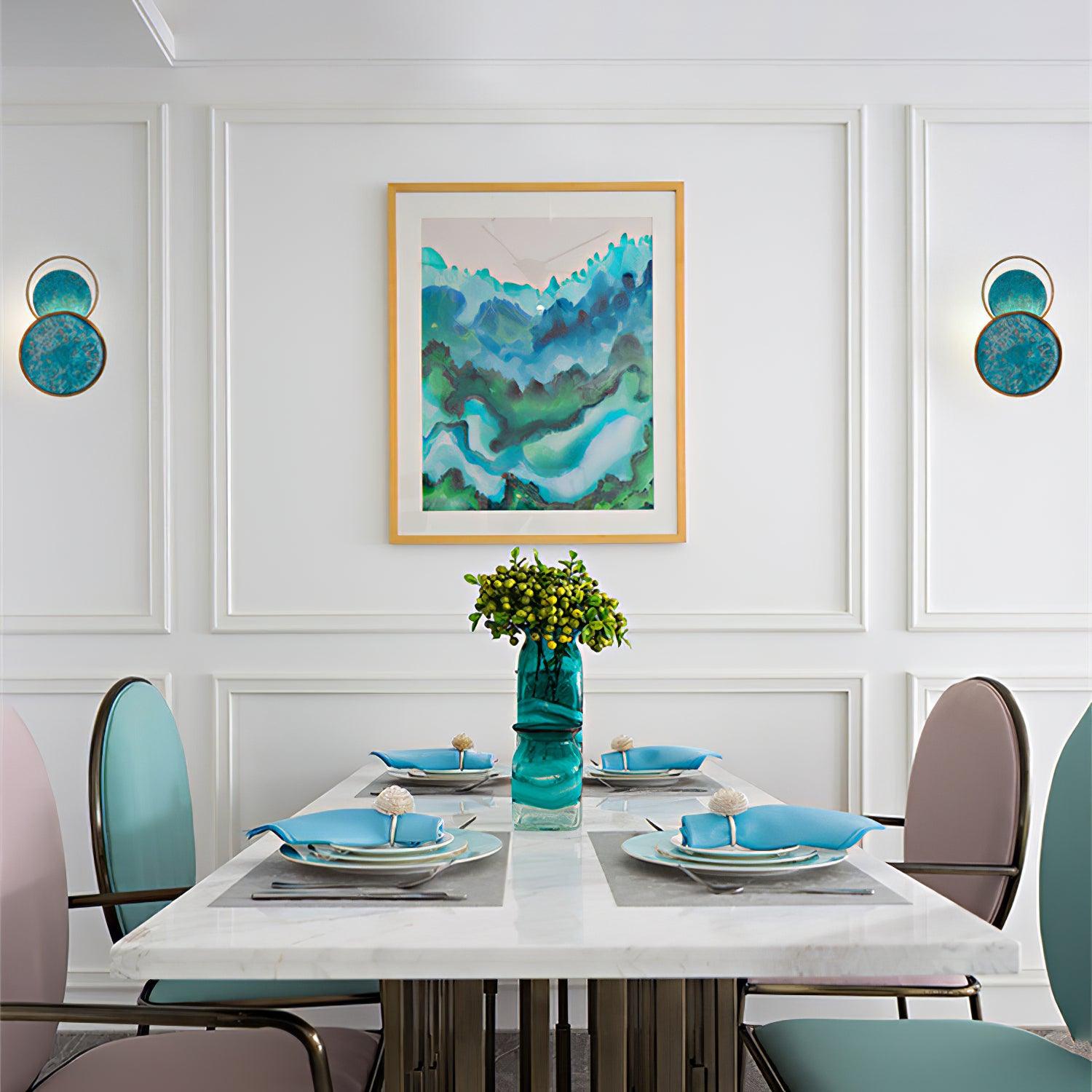 Pair of Turquoise Satellite lights flanking blue-green framed art above a dining table with turquoise napkins and chairs.