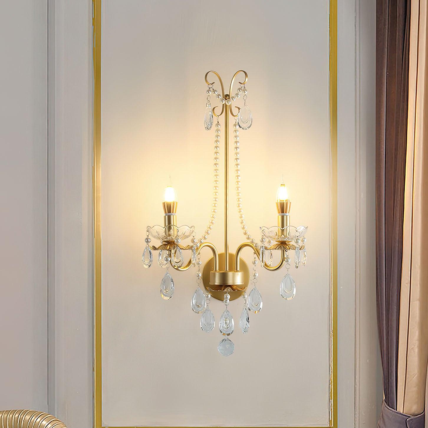 Gold wall light with glowing candle bulbs and clear drops in a gold-bordered panel beside gathered beige and brown curtain