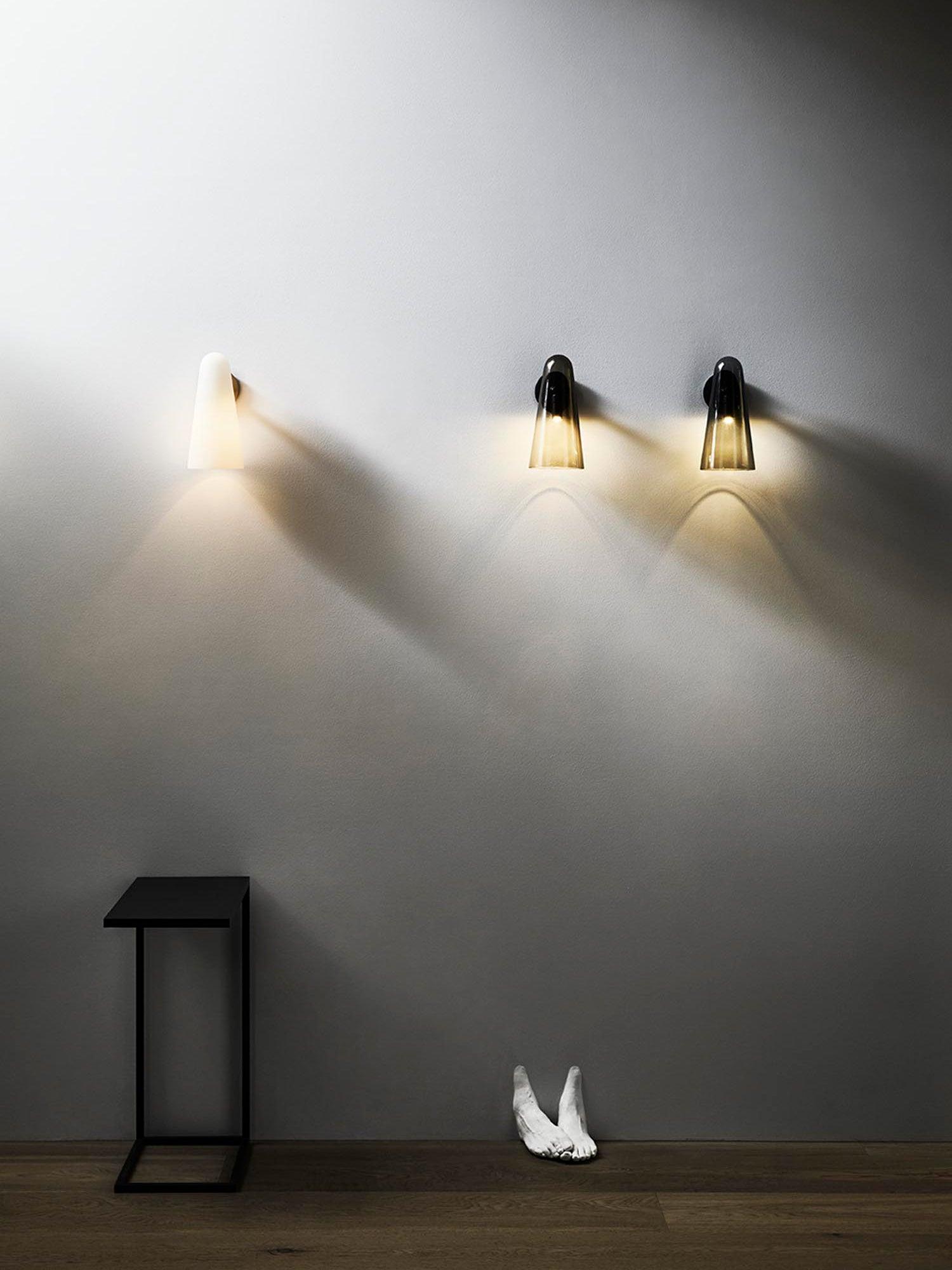 Three lit conical wall lights across a pale wall above a narrow dark side table