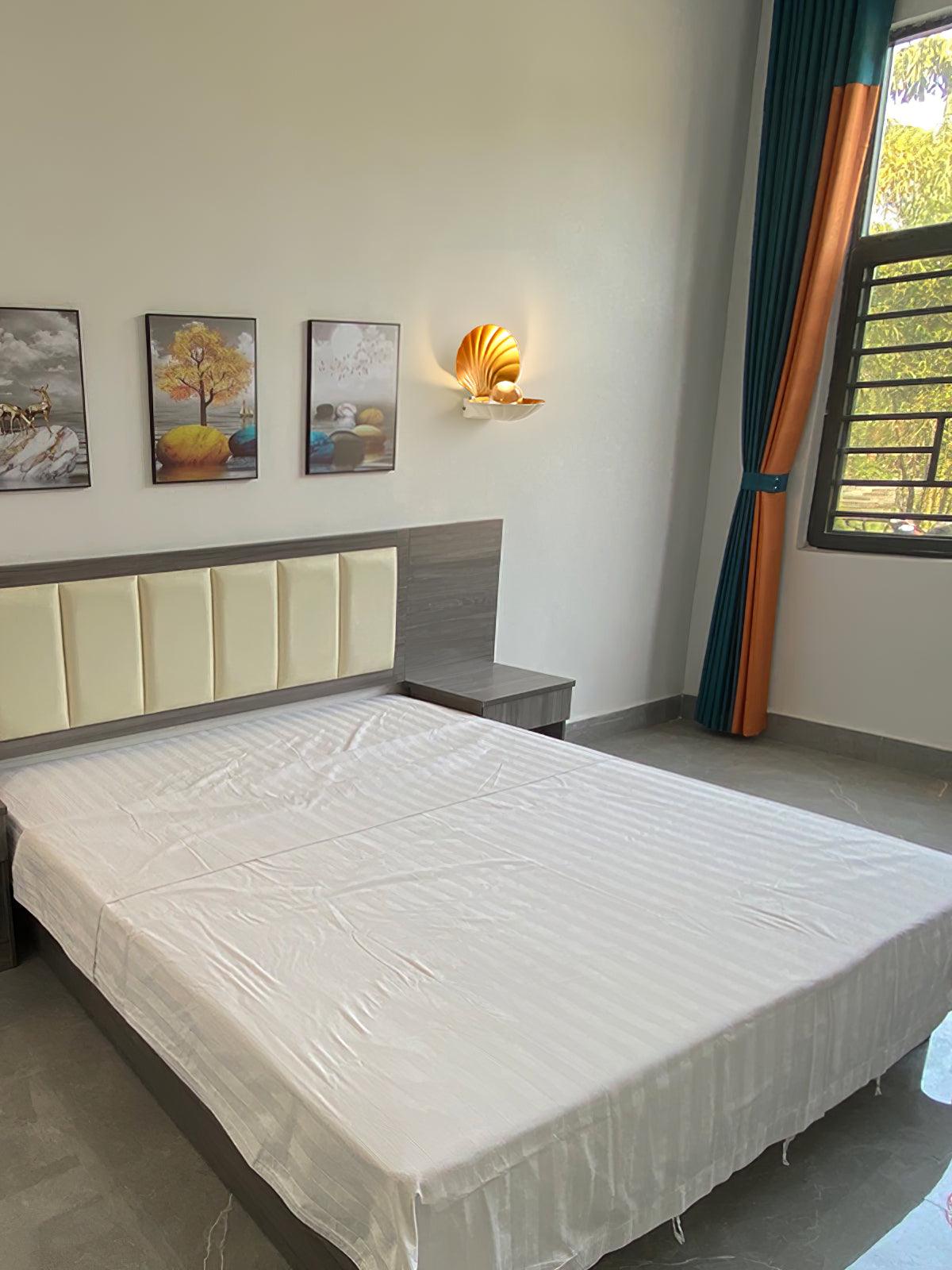 White shell wall light above a grey headboard near framed artwork and a window