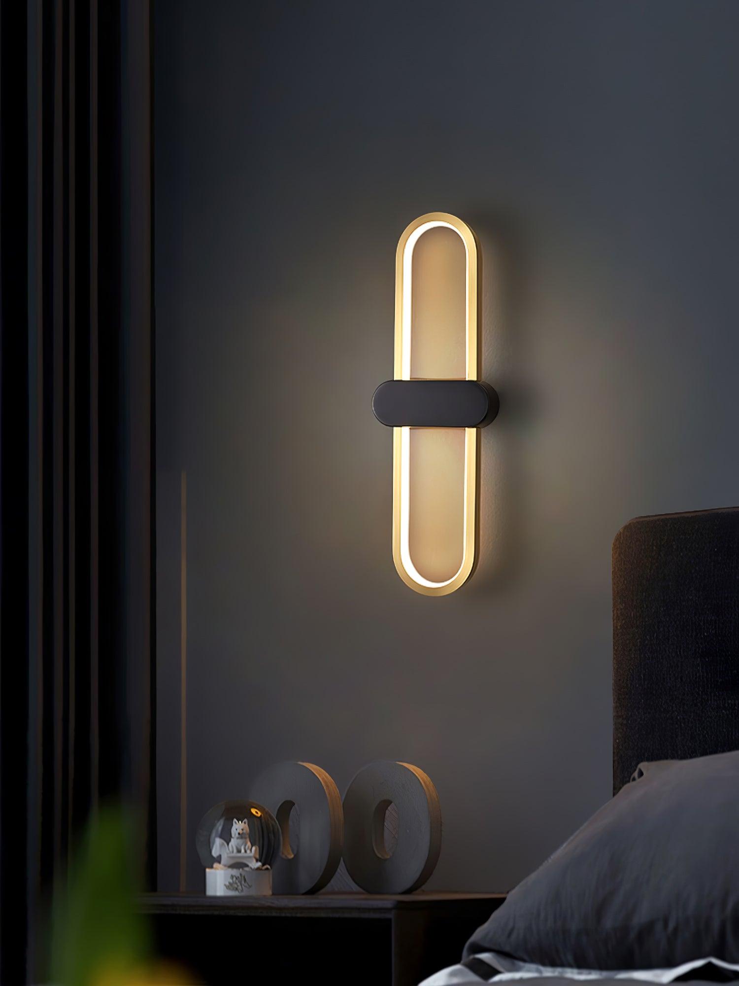 Gold oval wall light with black centre on a dark bedroom wall above wooden ornaments
