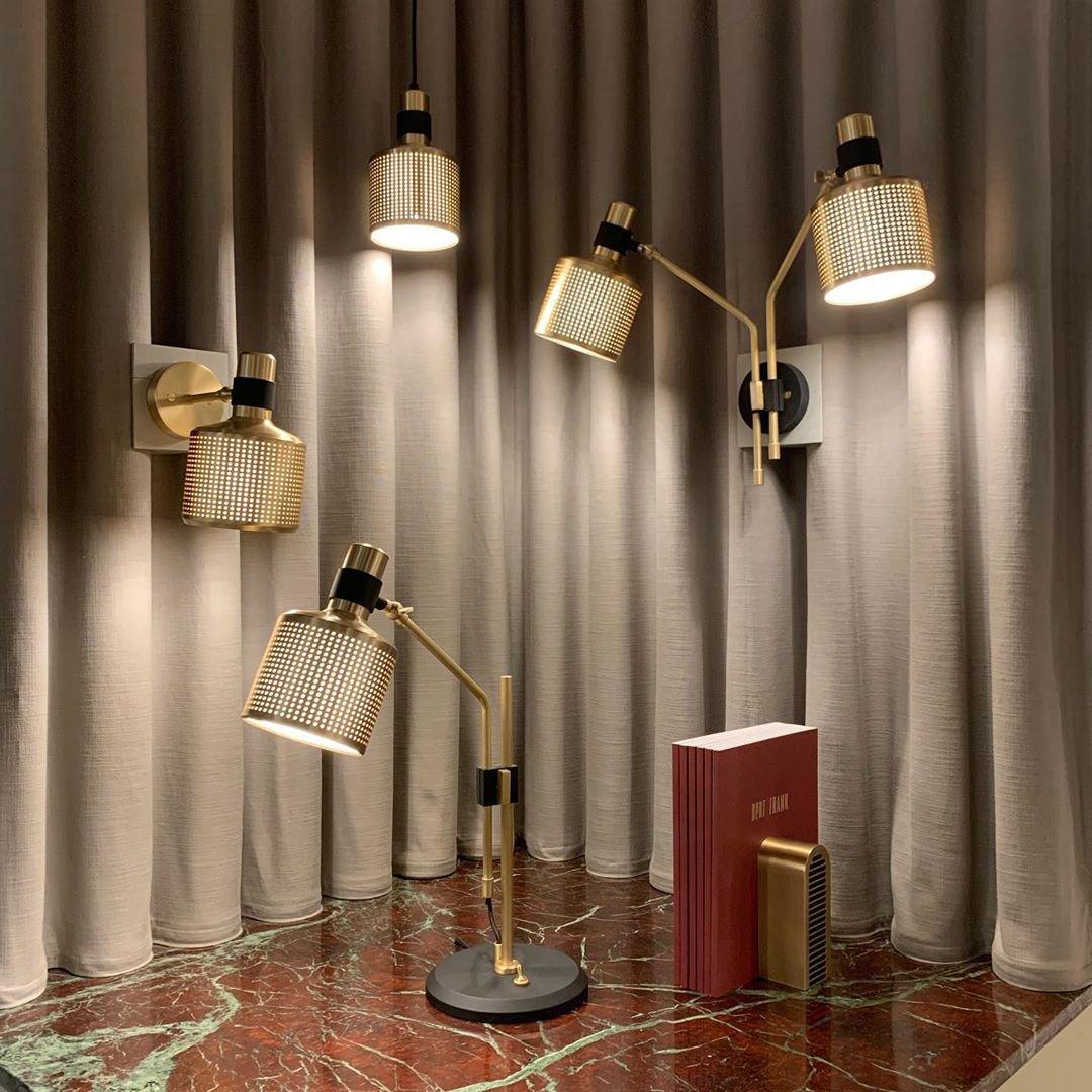 Gold-and-black single-head table lamp on a marble counter beside a book, with other pendant and wall lights in the display