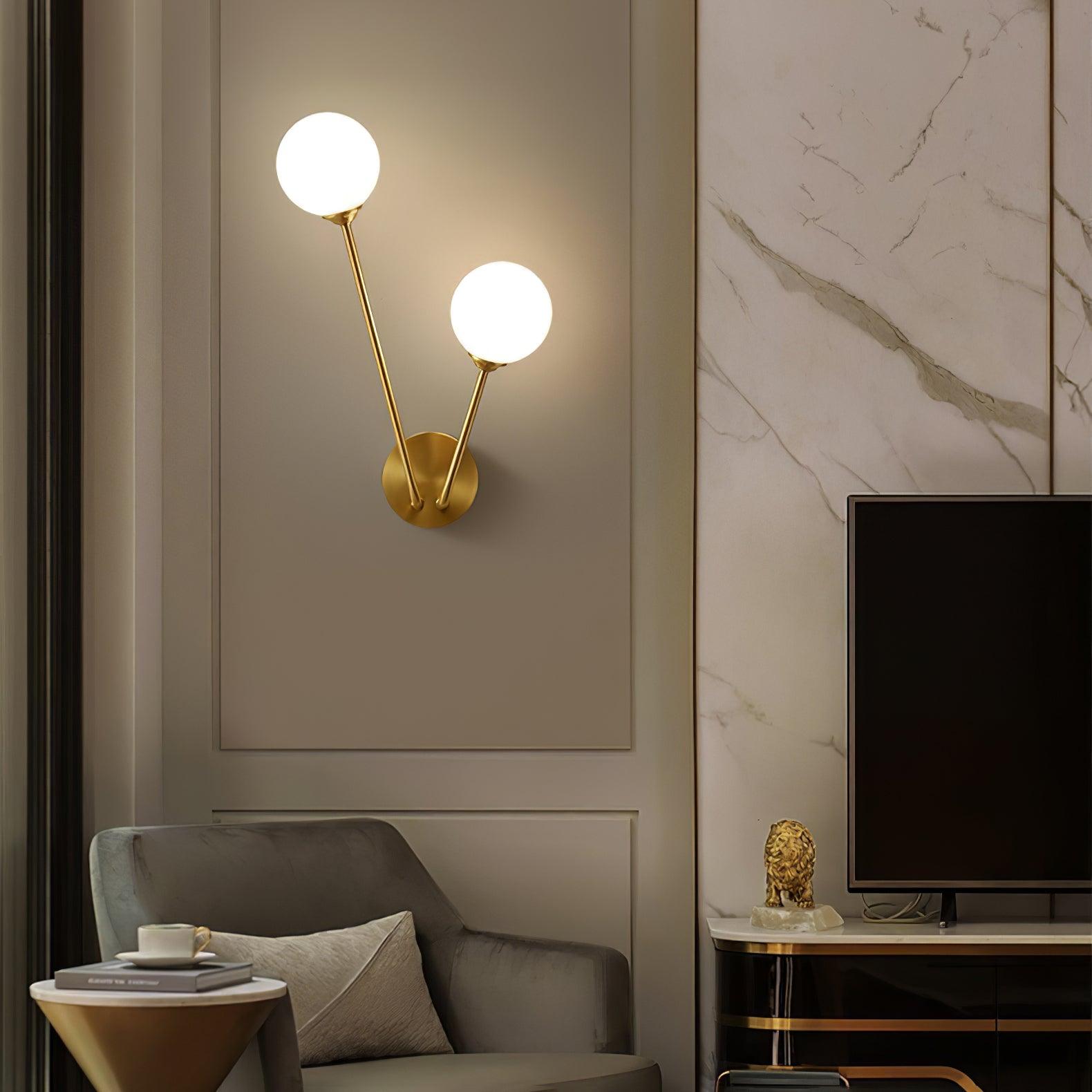 White two-globe light on moulded wall above grey seating, beside a television stand and gold ornament