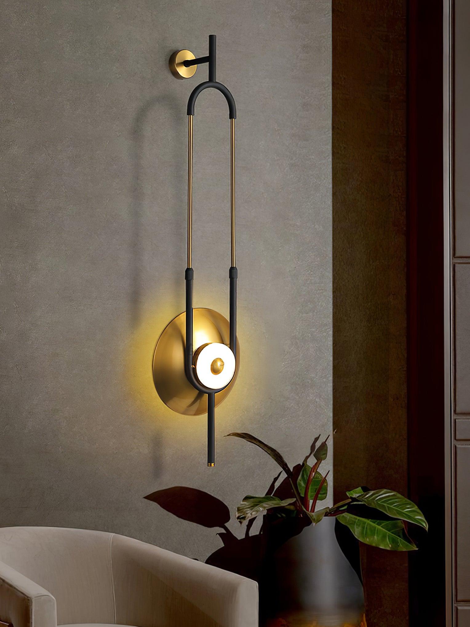 Oblique lit wall light above pale chair beside green-and-burgundy foliage in dark vase on textured wall