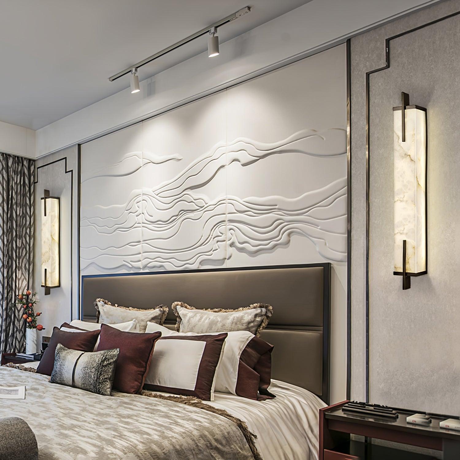 Two illuminated Calliope wall lights flanking an upholstered bed beneath wavy wall artwork