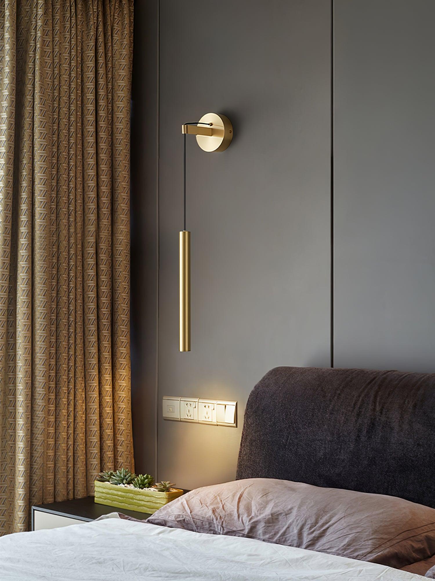 Brass-coloured cylinder light above a bedside surface with sockets, planter and patterned curtains